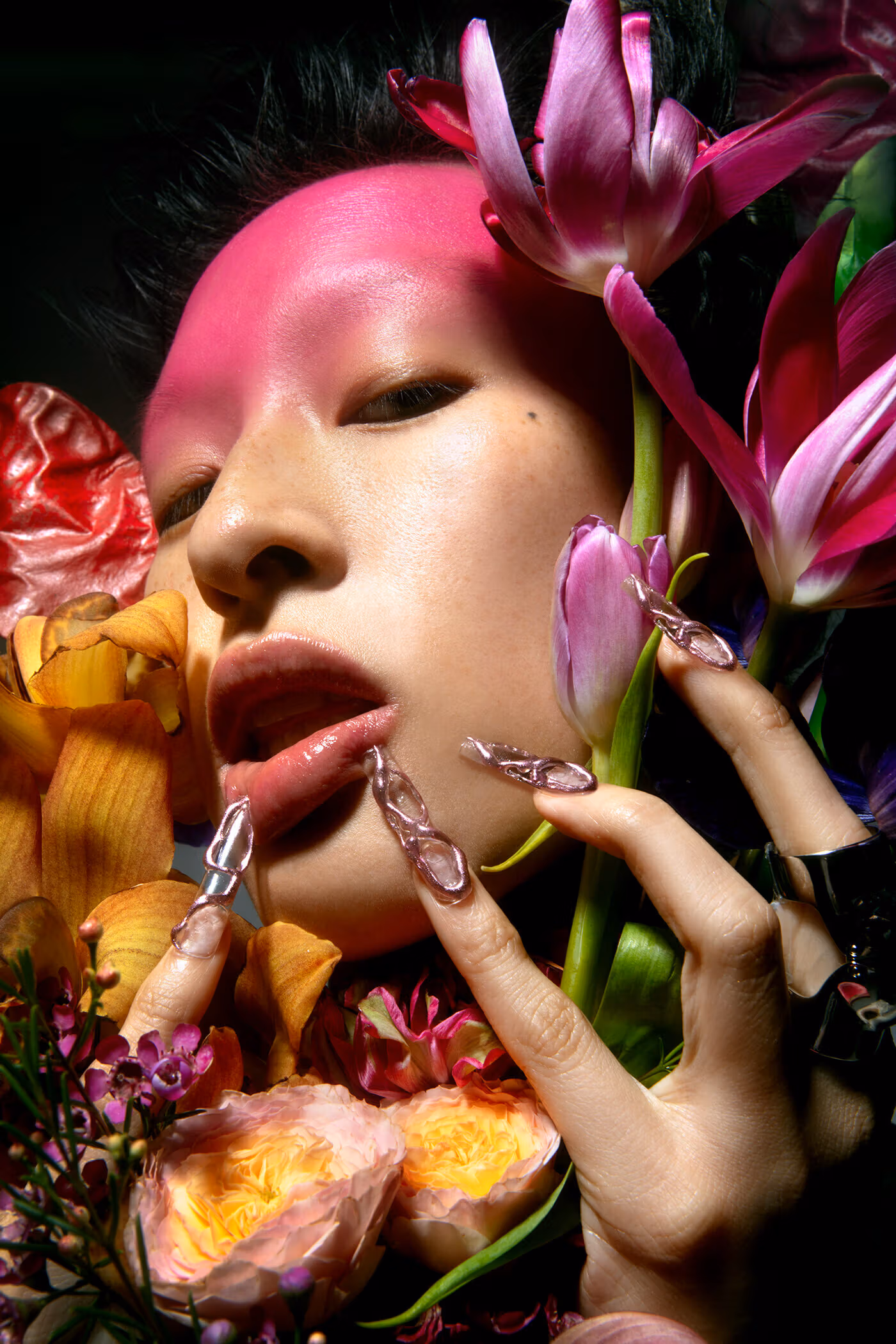 Close up portrait of a person with long nails holding several flowers close to their face.