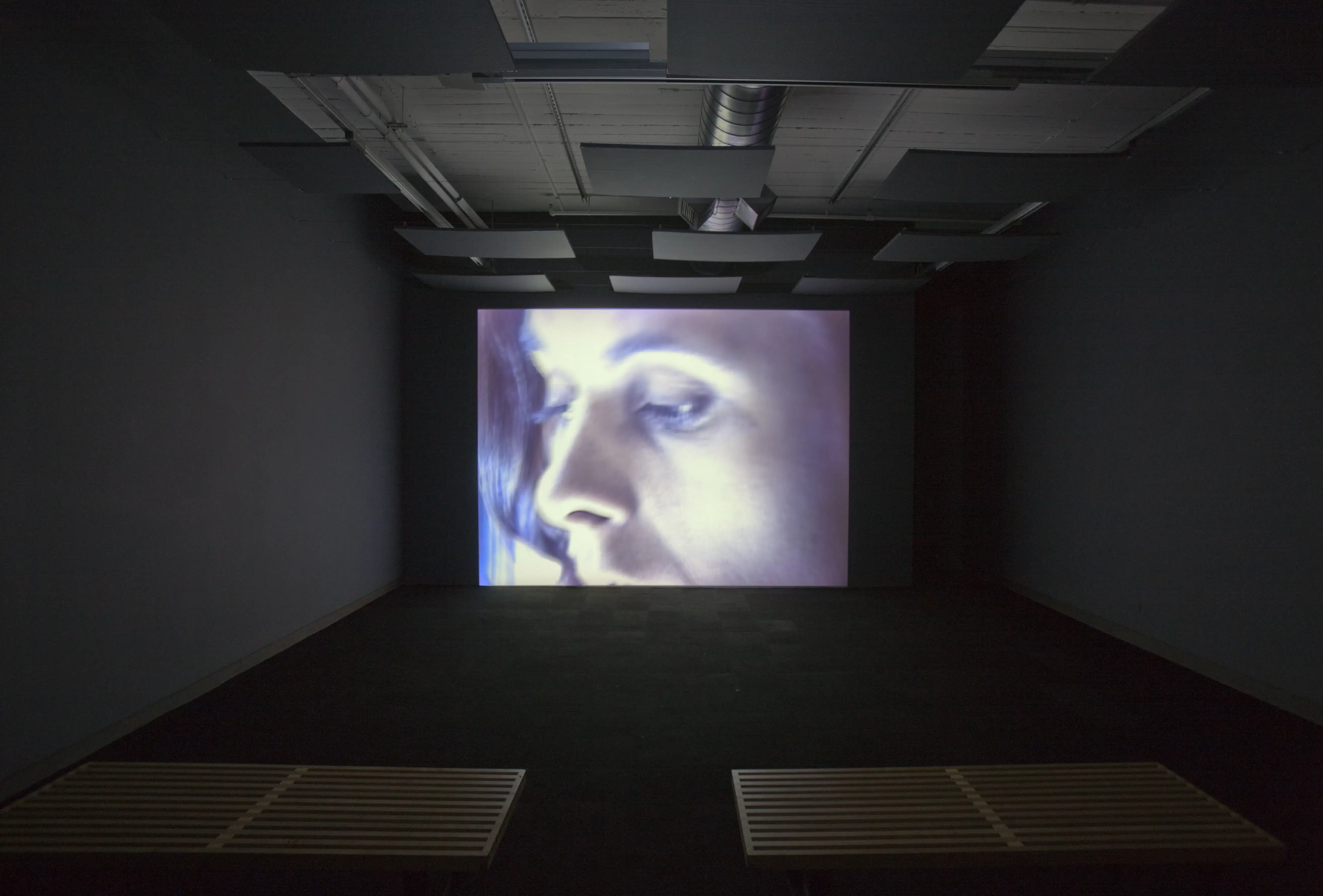 A screen in a dark room glowing with a woman's face.