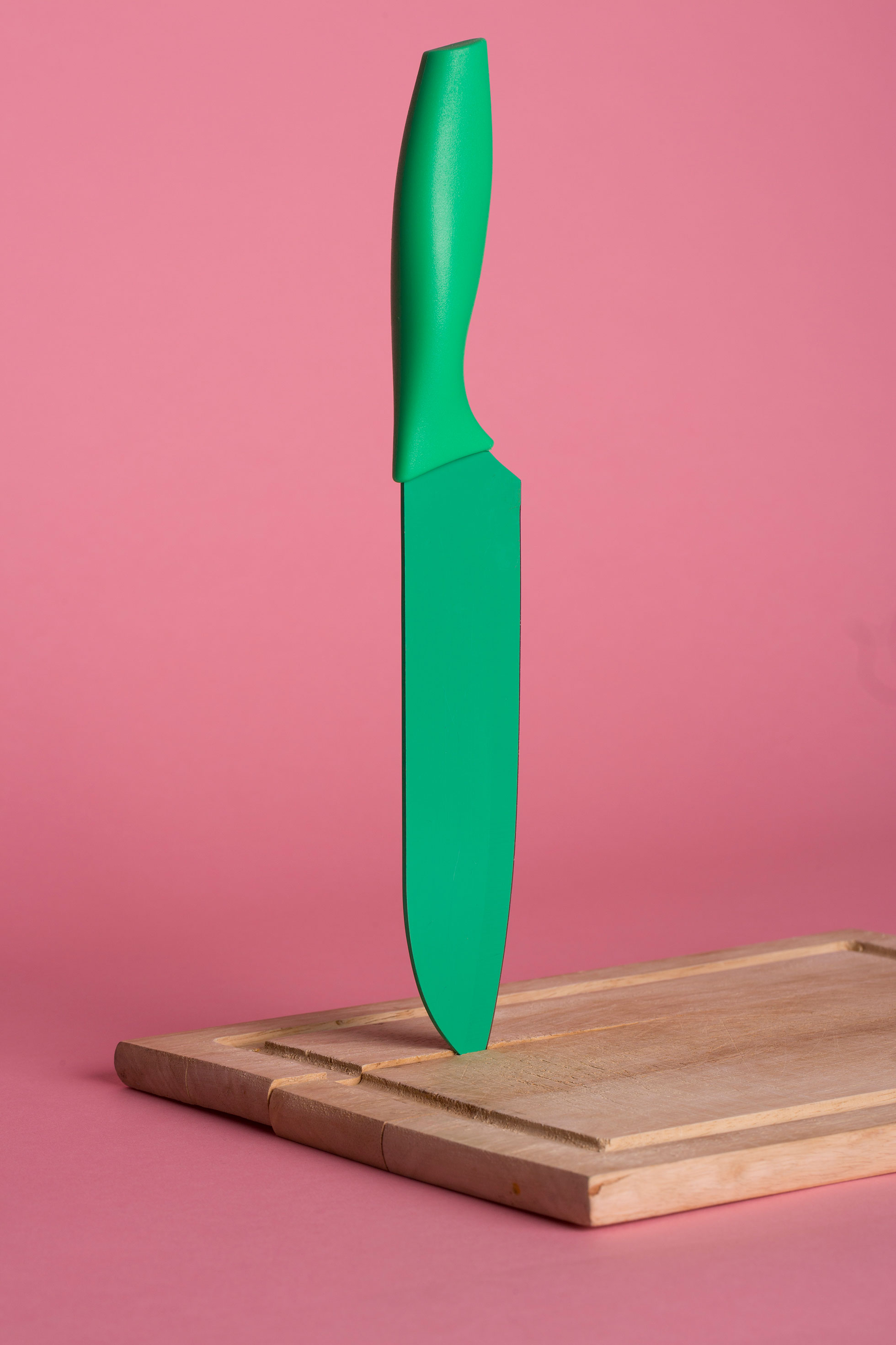 A green knife suspended in a wooden cutting board.