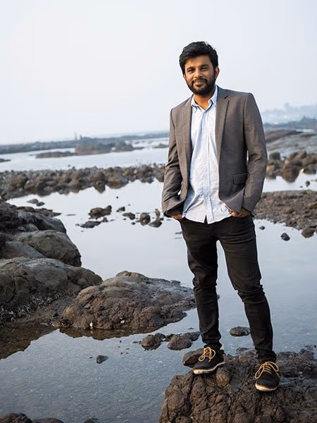 There is a man standing on rocks with water below him. He is looking forward and smiling.