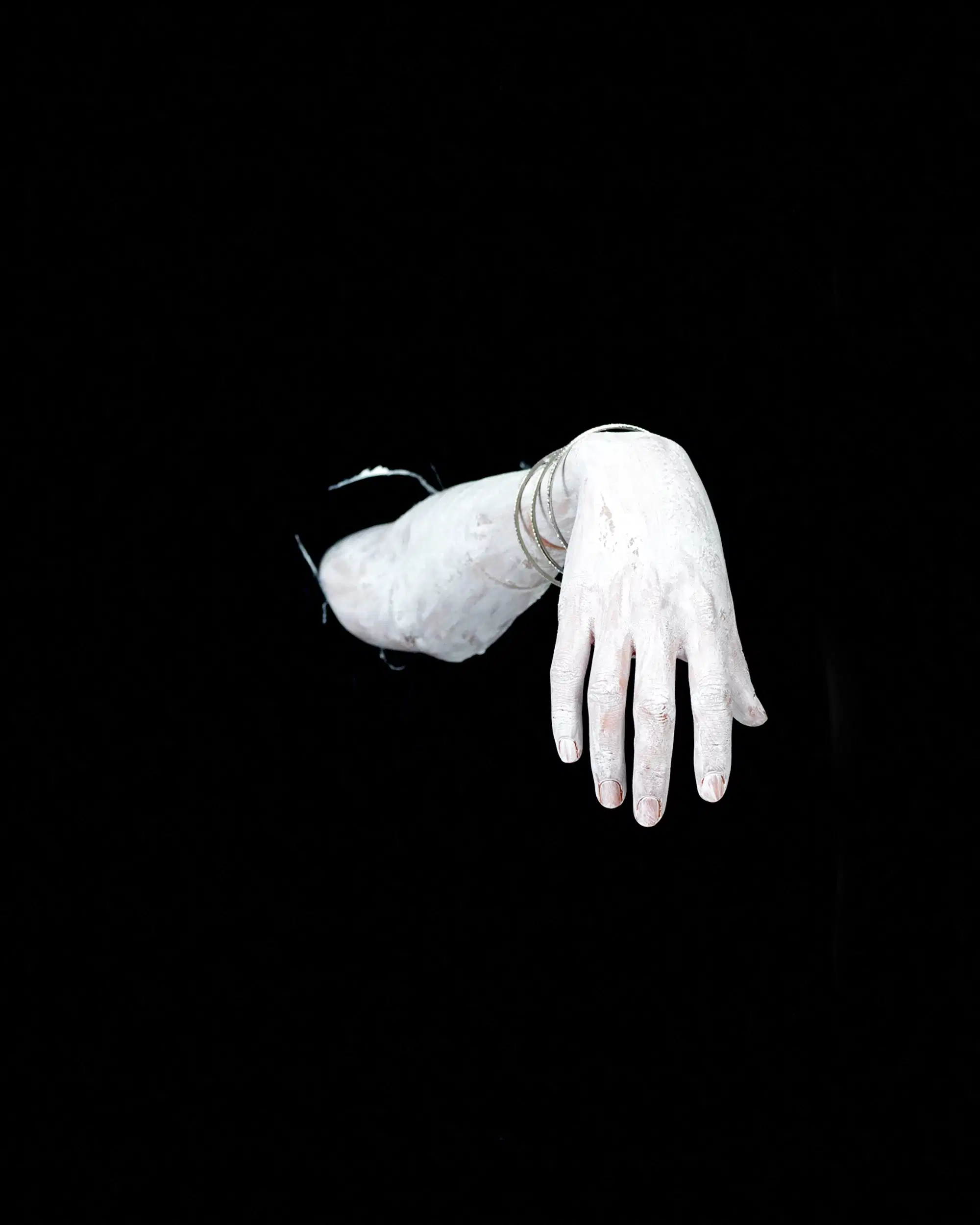 A hand and forearm emerging from darkness, covered with white paint.