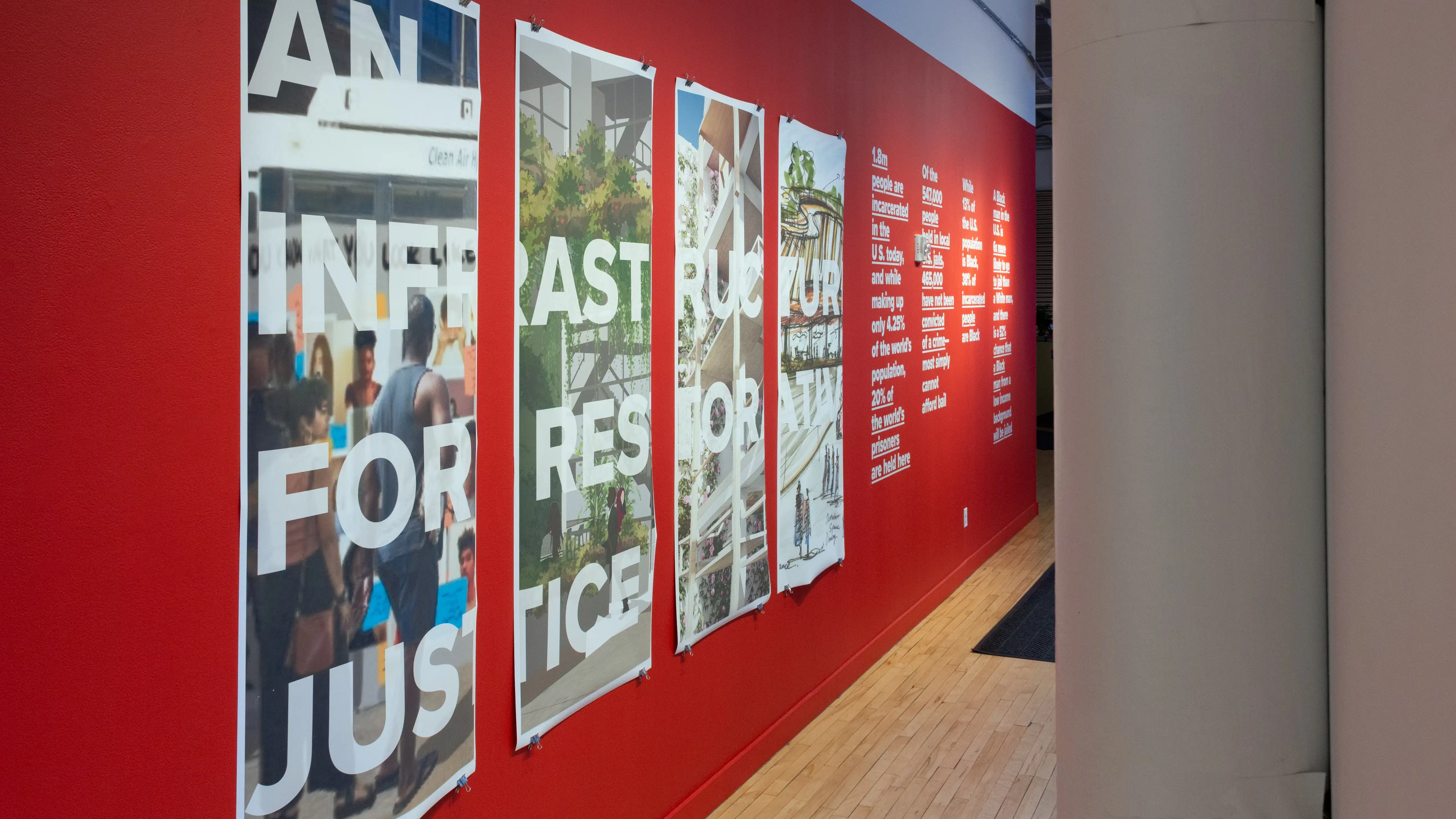 Exhibition view of An Infrastructure for Restorative Justice, featuring hallway painted red with a large posters and text on the wall.