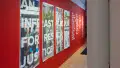 Exhibition view of An Infrastructure for Restorative Justice, featuring hallway painted red with a large posters and text on the wall.