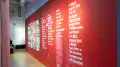 Exhibition view of An Infrastructure for Restorative Justice, featuring hallway painted red with a large posters and text on the wall.