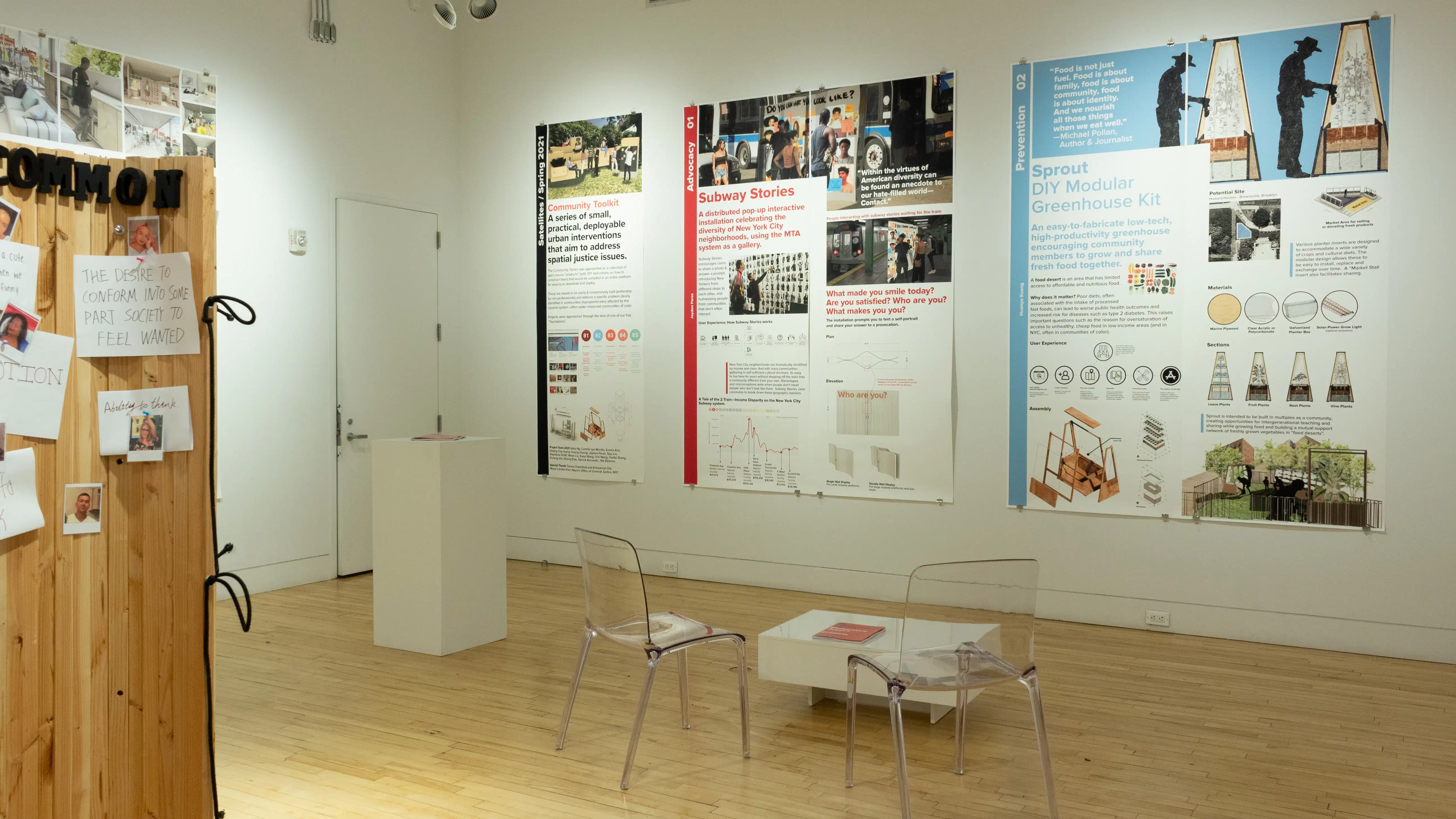 Exhibition view of An Infrastructure for Restorative Justice, featuring wooden sculpture, table, 2 clear chairs, and large posters on the walls.