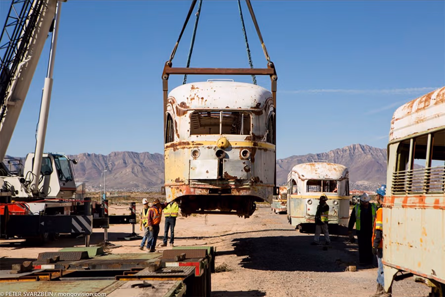 Rusty old train car being lifted by a crane with multiple construction workers around