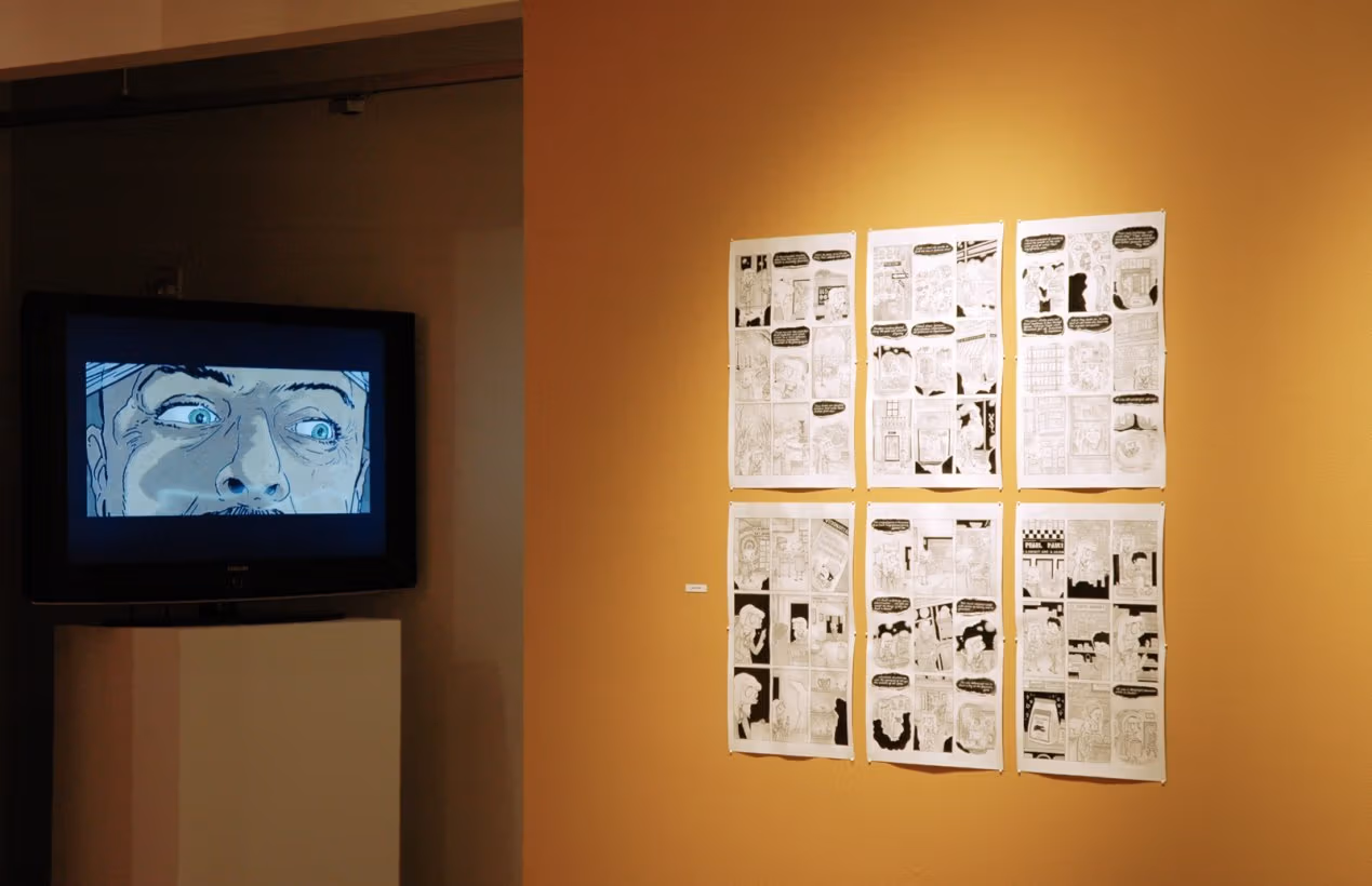 Photograph of golden yellow wall containing black and white comic pages next to a tv, on the left, showing an animated video with a close-up of a man's face visible on the screen.