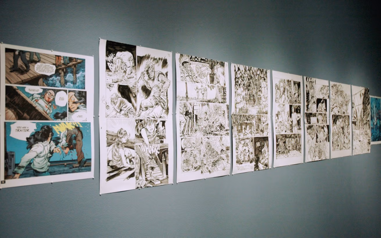 Photograph of comic book panels on paper pinned to a light teal wall.