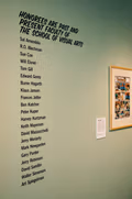 Exhibition wall text with partial list of artists next to a framed artwork.
