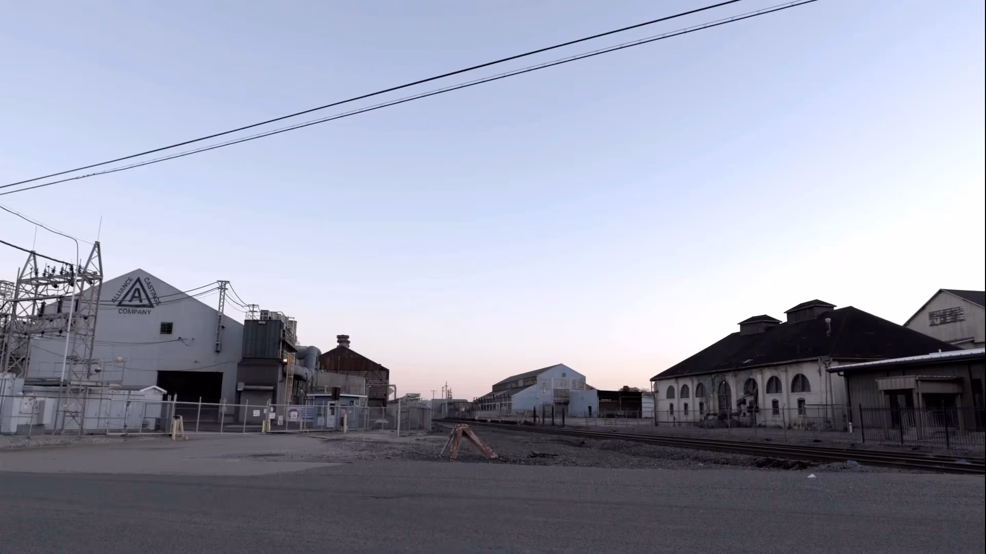 A wide urban landscape with a factory on the left.; the sun is low in the sky