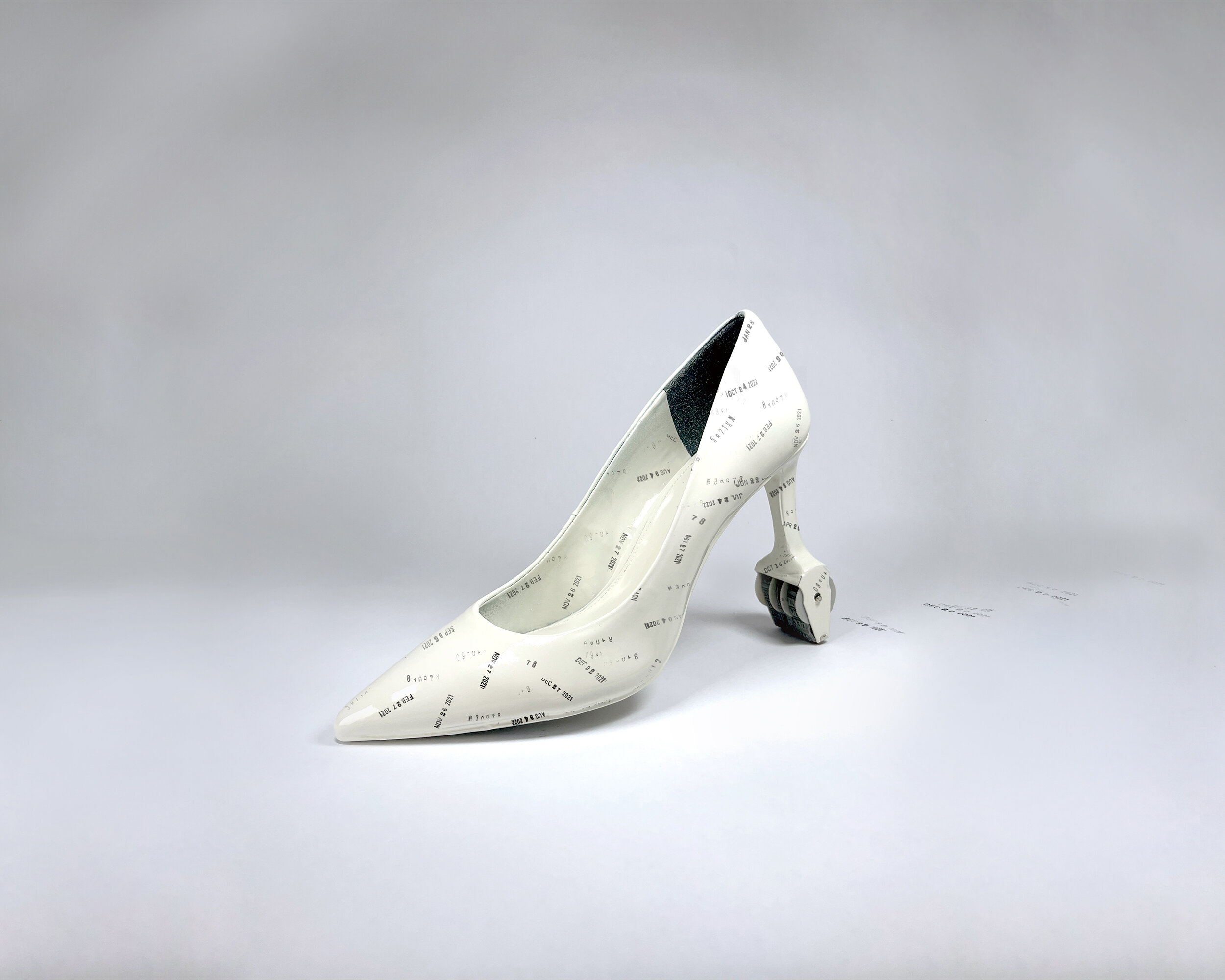 On a grey backdrop is a white high heel stiletto speckled with stamped dates, the heel of the shoe is a date stamp