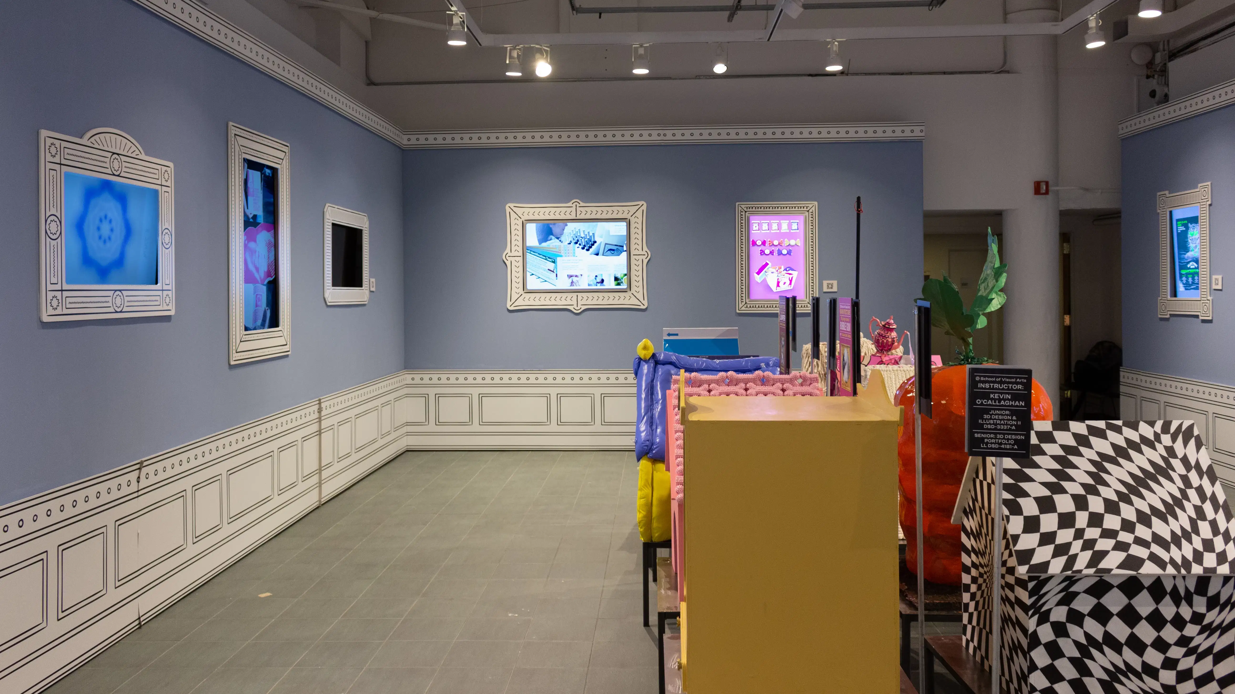 Installation image featuring a large room with ten dog house sculptures in the center and six framed monitors visible on the walls.