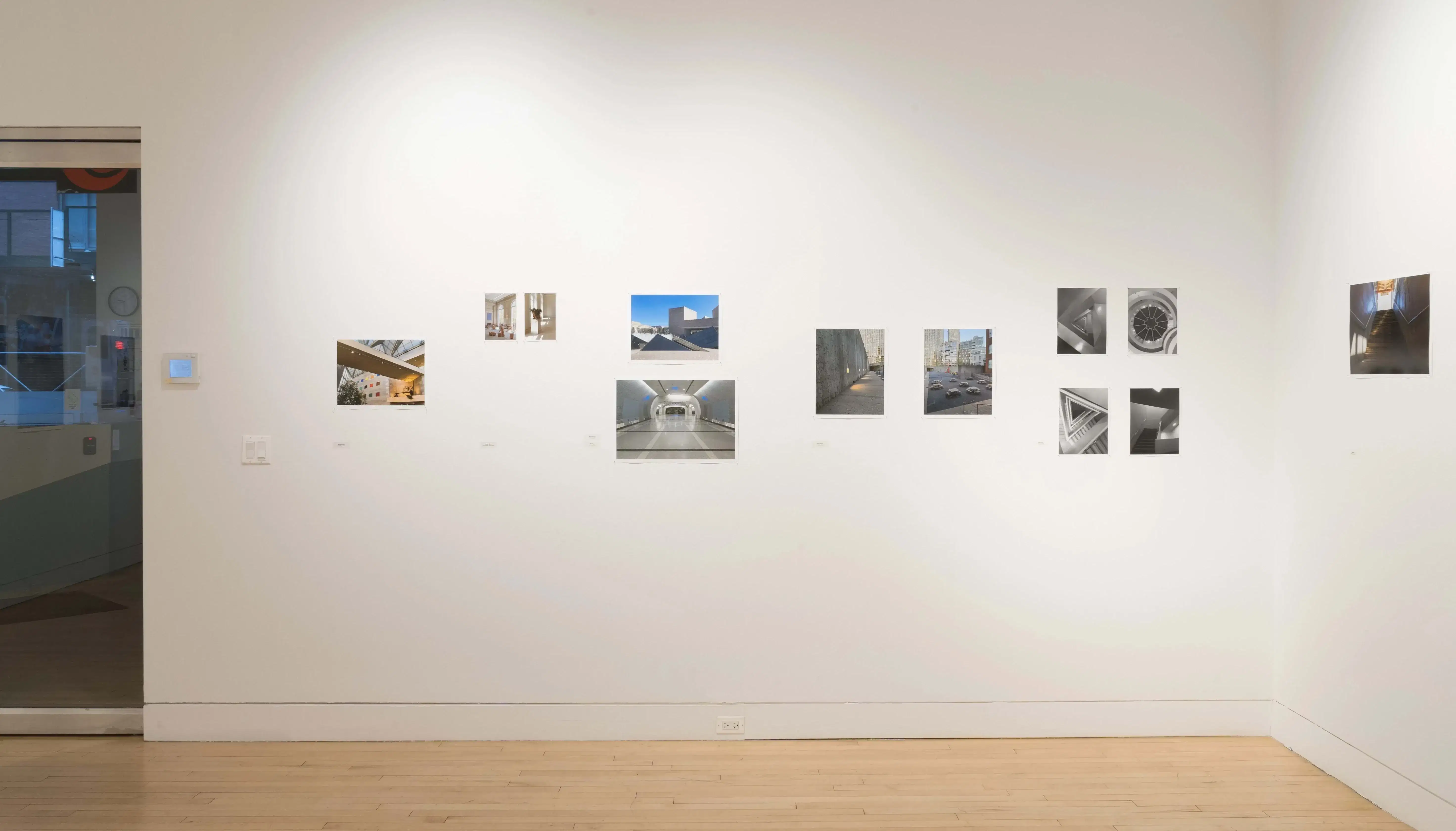 Straight shot of one wall in the Flatiron Gallery, showing multiple prints of industrial moments in varying sizes lining the walls, and a set of glass doors to the right.