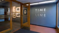 Photograph from just outside lobby gallery of Visual Arts Museum with exhibition text, "Time Line: Sheila Metzner" on the wall to the right, on the left inside gallery are several framed photographs.