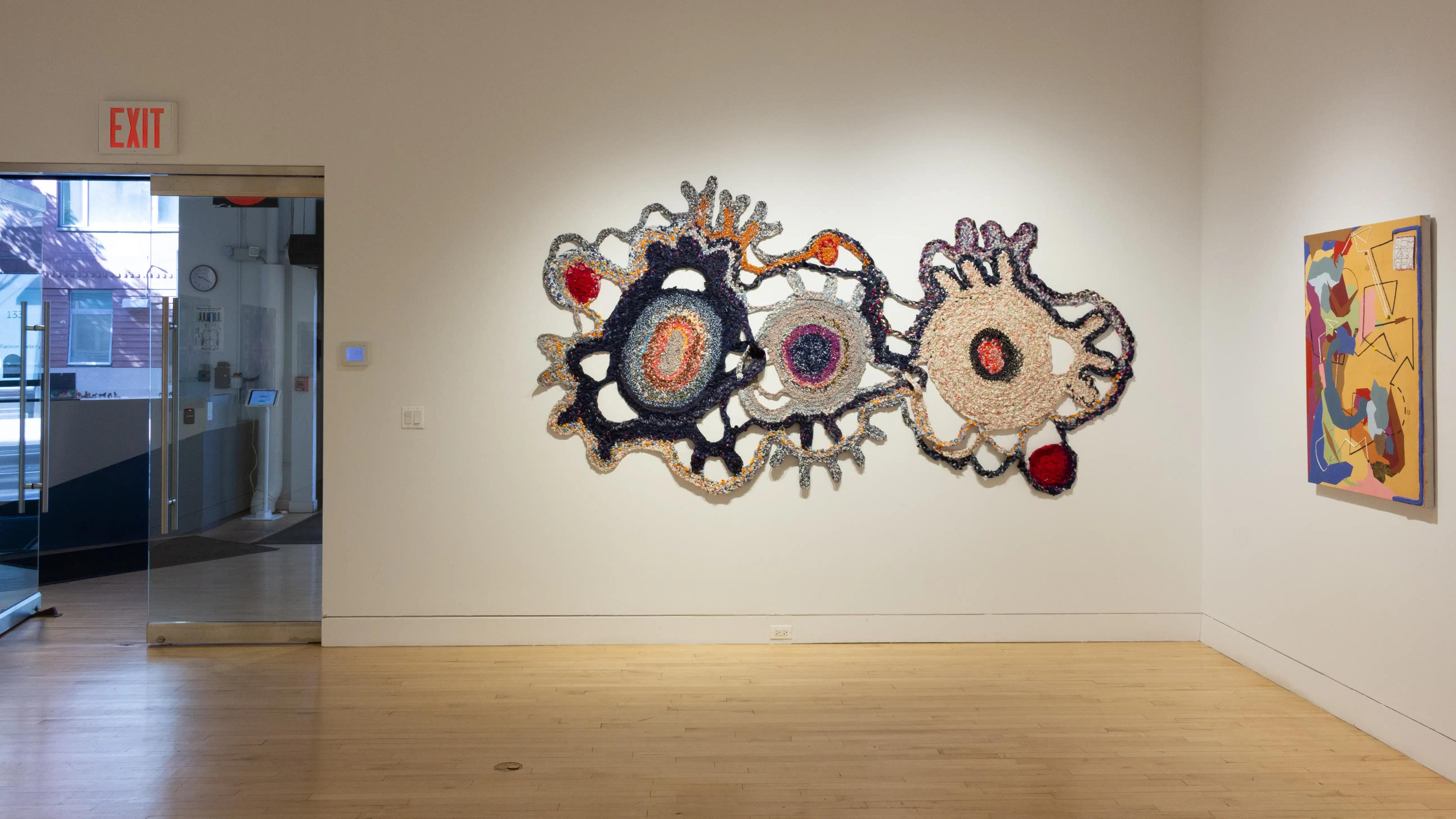 Installation image featuring one mixed media 2d work and one textile work, with the gallery doors to the left.