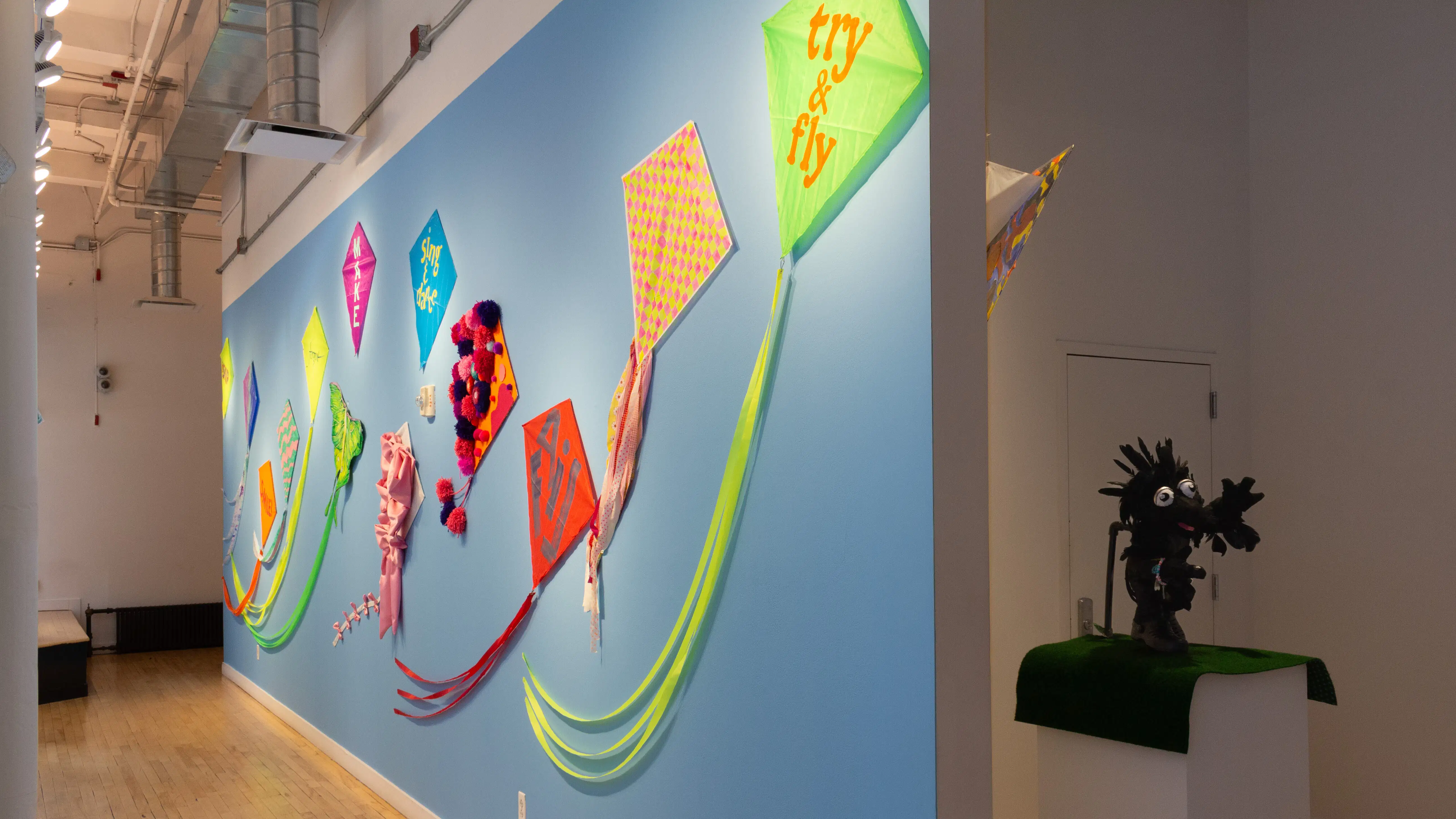 Thirteen kites hung on a long gallery hallway wall. 