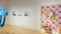 On the left, three artworks hang from a wall depict a person in mid-air, and on the far right, an artwork installation depicts an interior bedroom-like space with floral wallpaper.