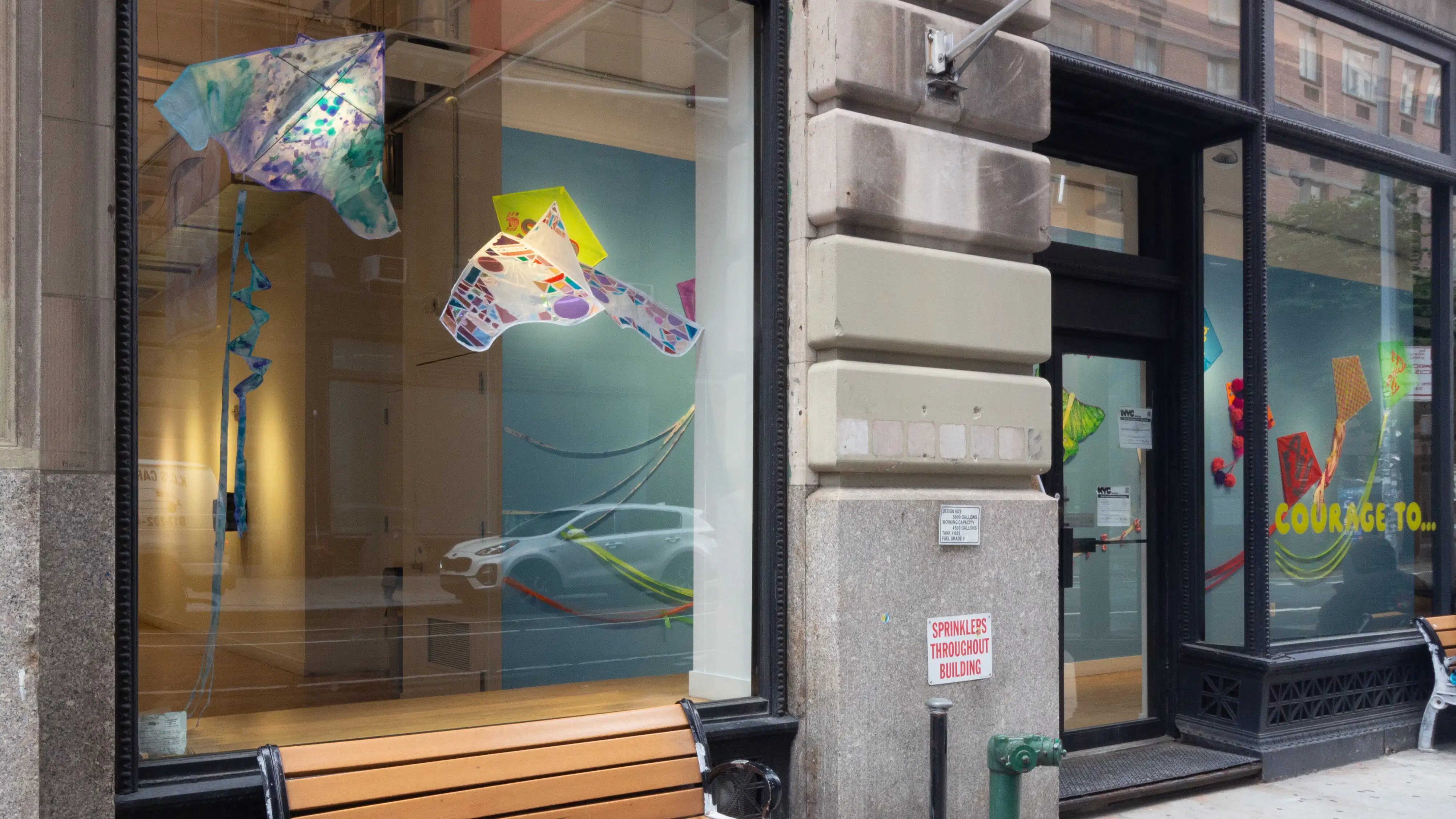 Streetview into large window where two colorful kites are suspended above a platform.