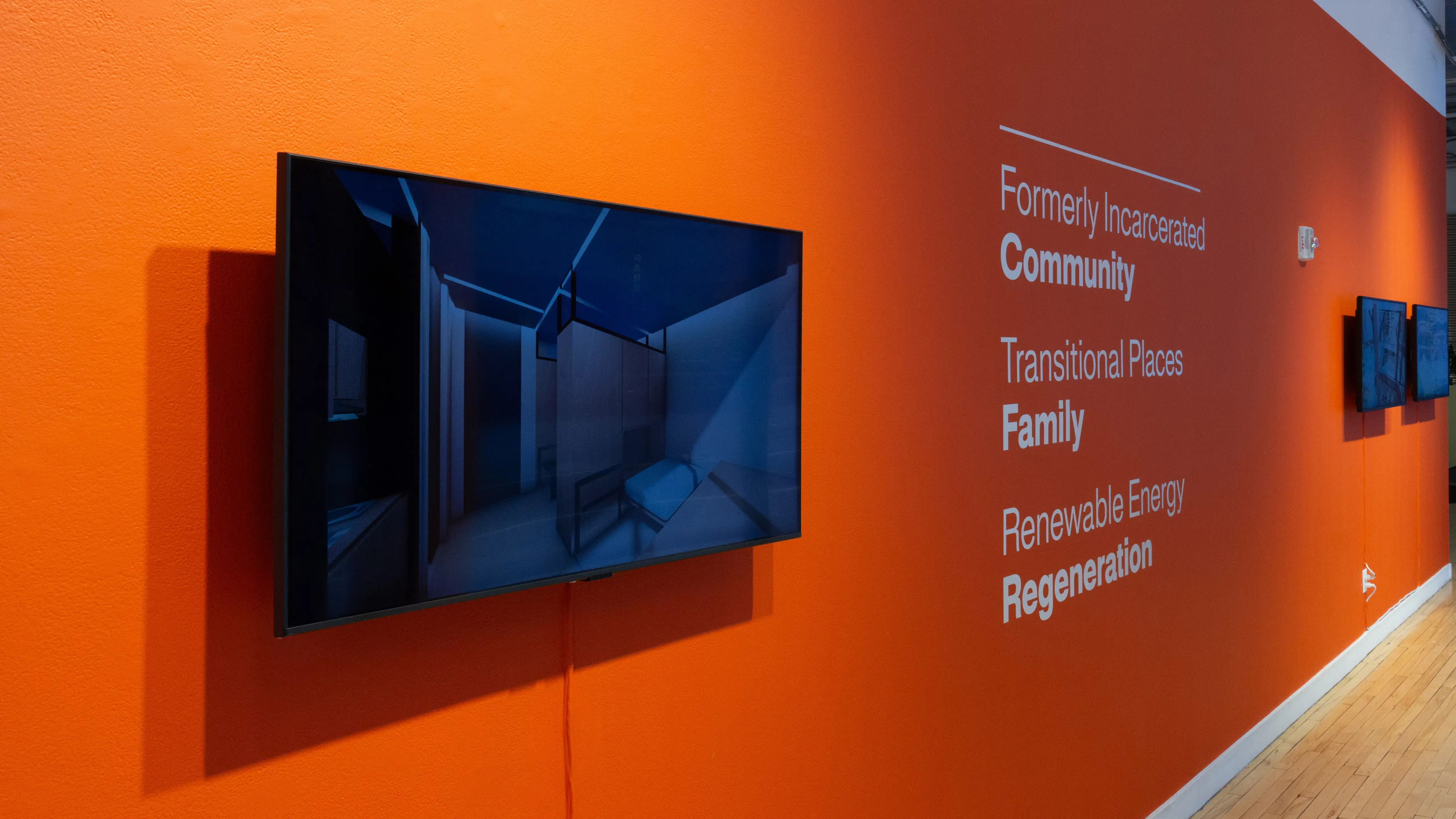 Installation image of an angled view of an orange wall with text and three monitors.