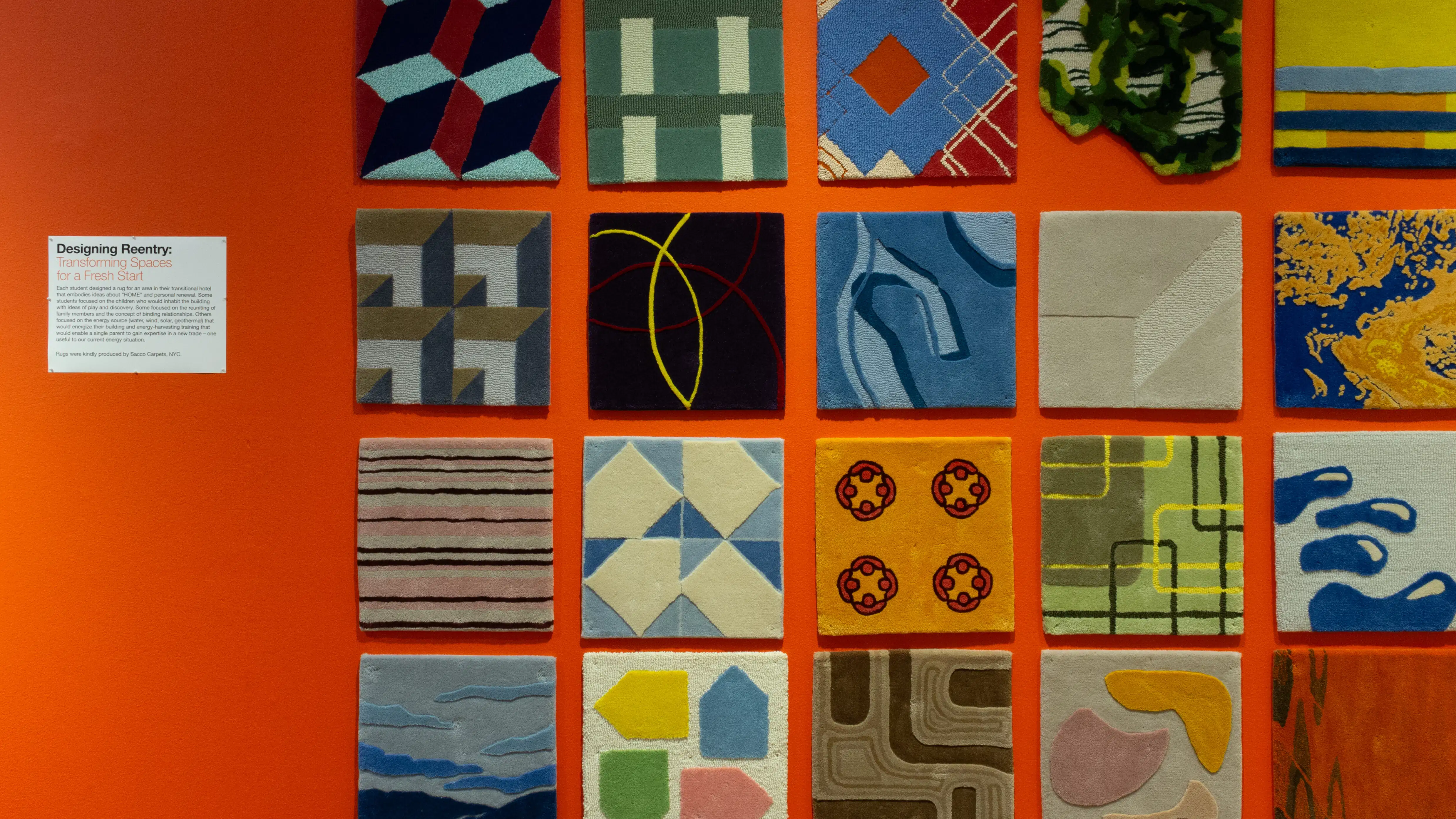 Installation image of a straight view of an orange wall with carpet squares of differing patterns.