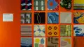 Installation image of a straight view of an orange wall with carpet squares of differing patterns.