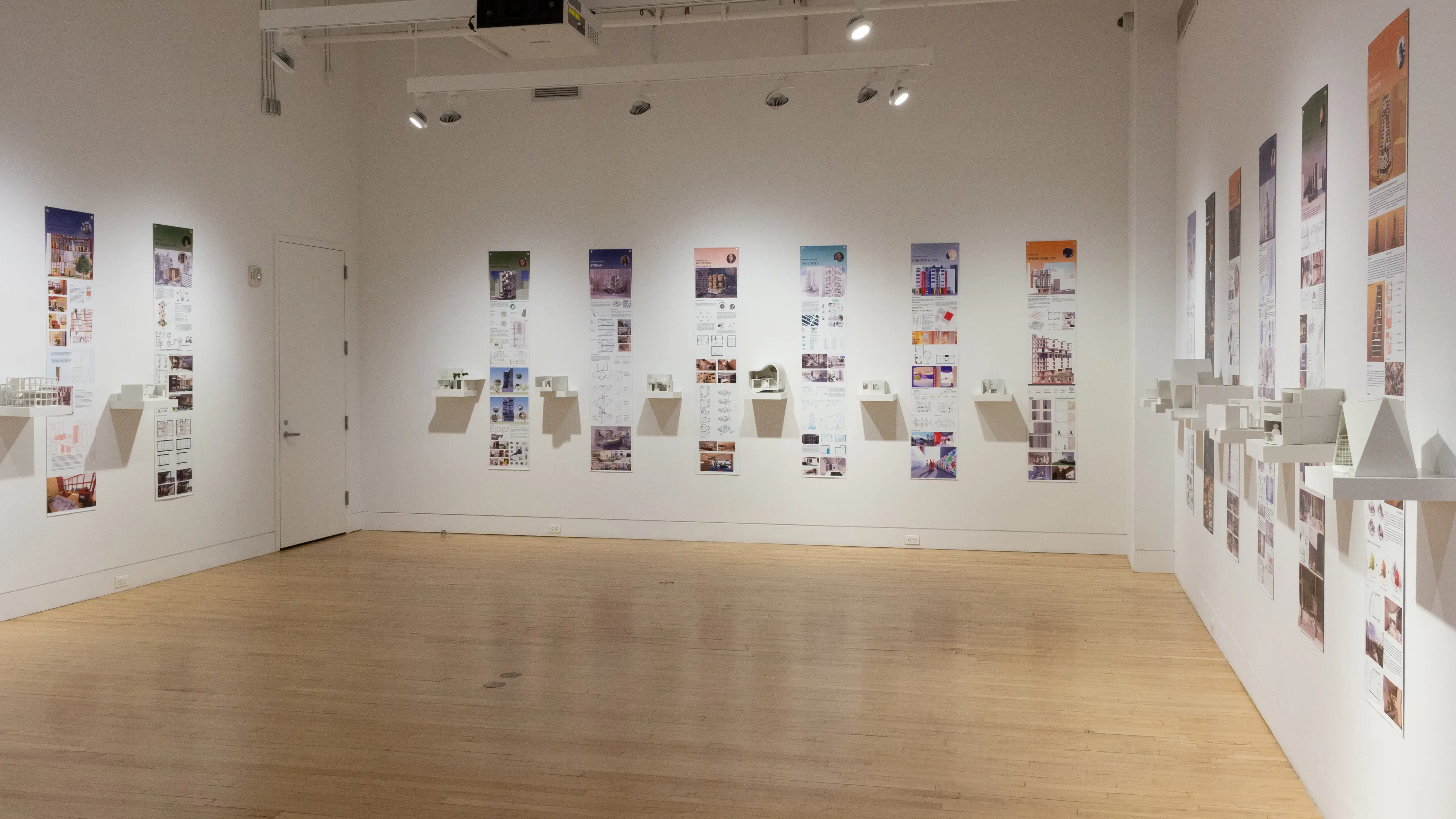 Installation image showing a three walls of a large gallery with building models on shelves, and information banners for each to the right.