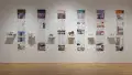 Installation image showing a straight view of a gallery wall with six building models on shelves, and information banners for each to the right.