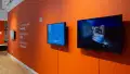 Installation image of an angled view of an orange wall with text and three monitors.