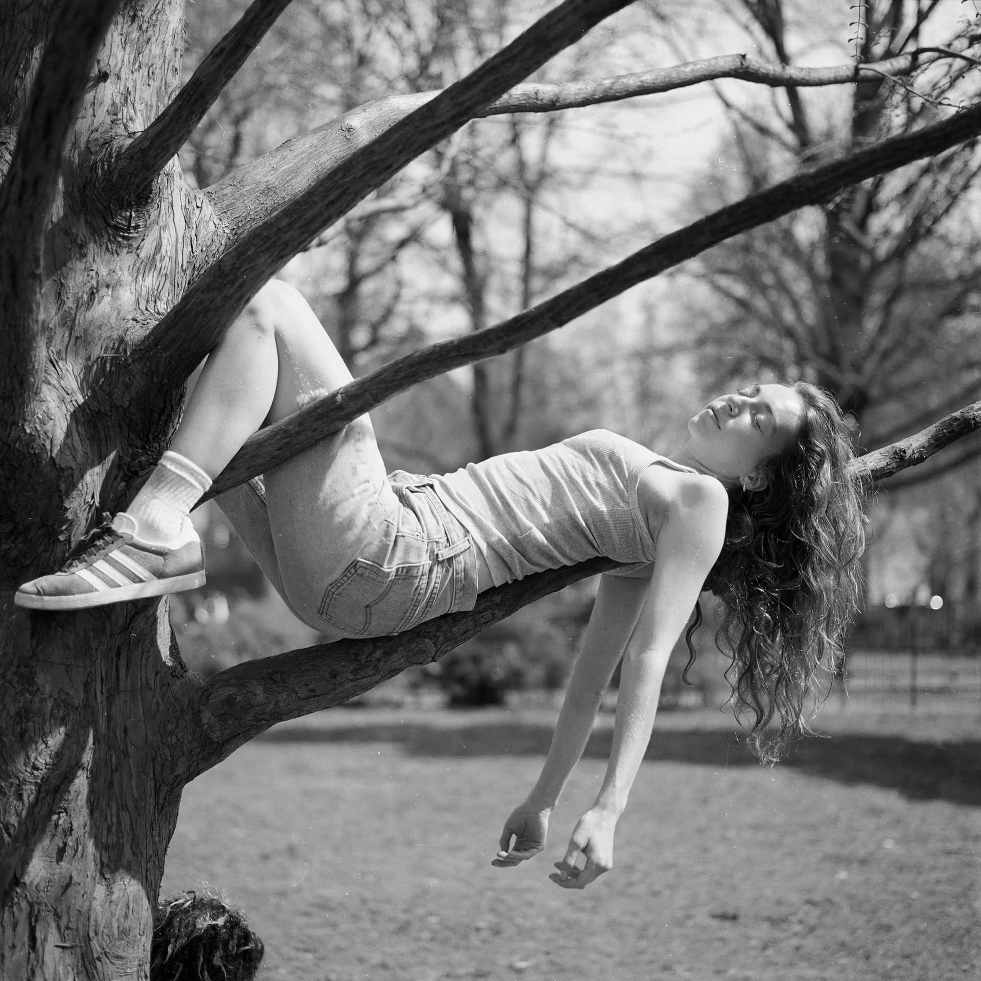 Black and white photograph of a girl resting on a tree branch.
