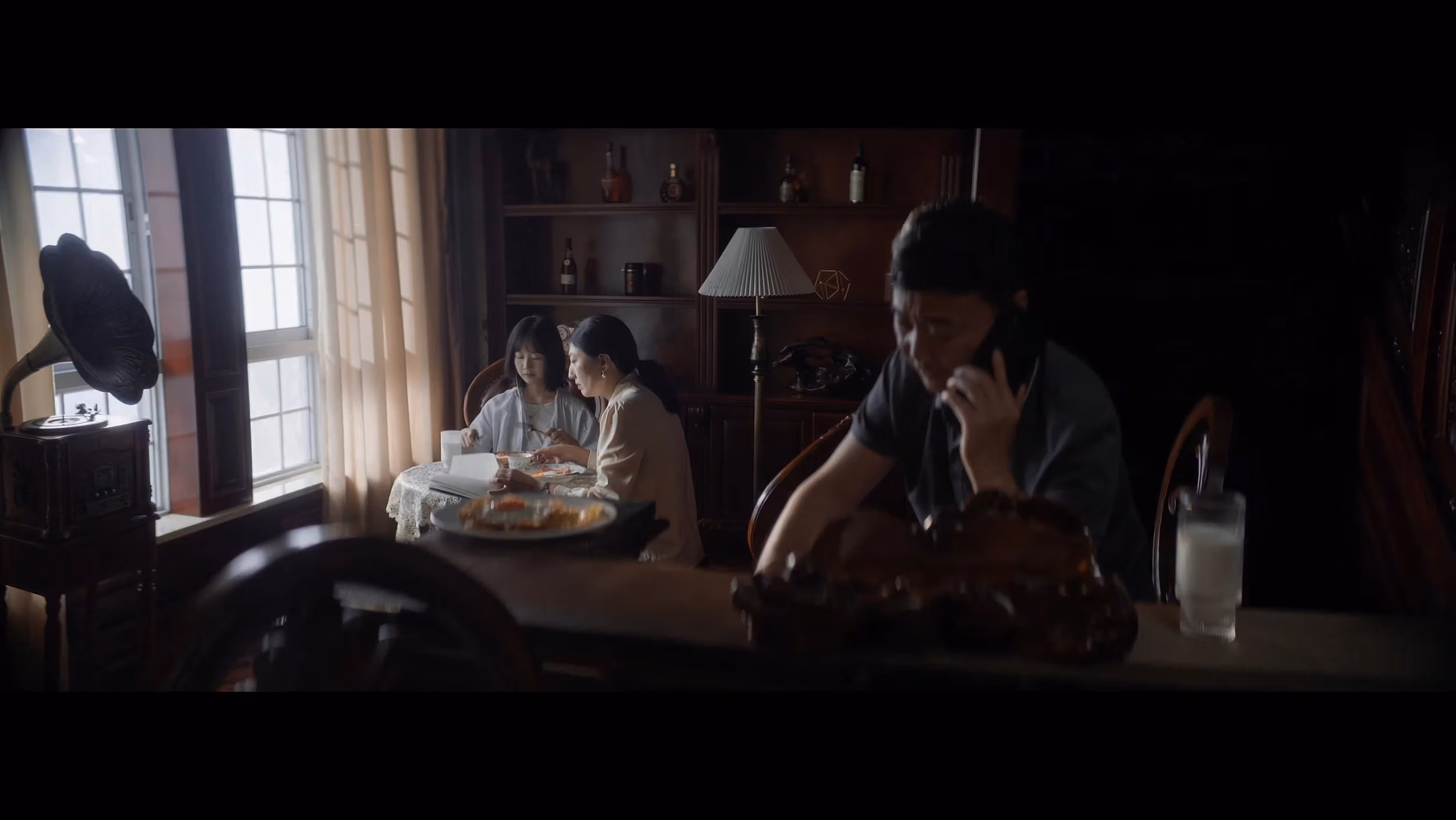 A man on a phone in a household. Two women sit at a table behind him.