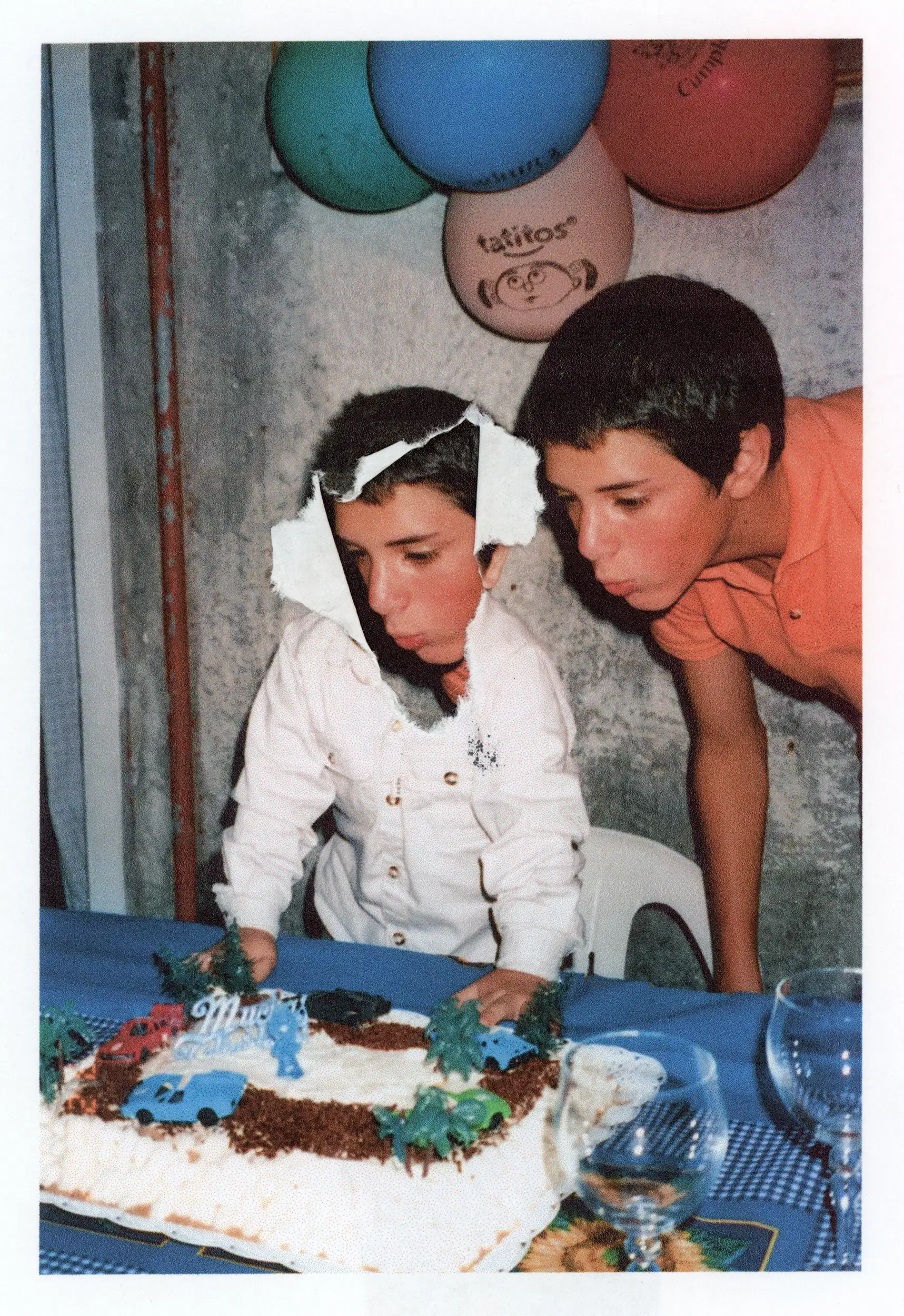 Color photograph of a child blowing out a birthday cake for a younger child.