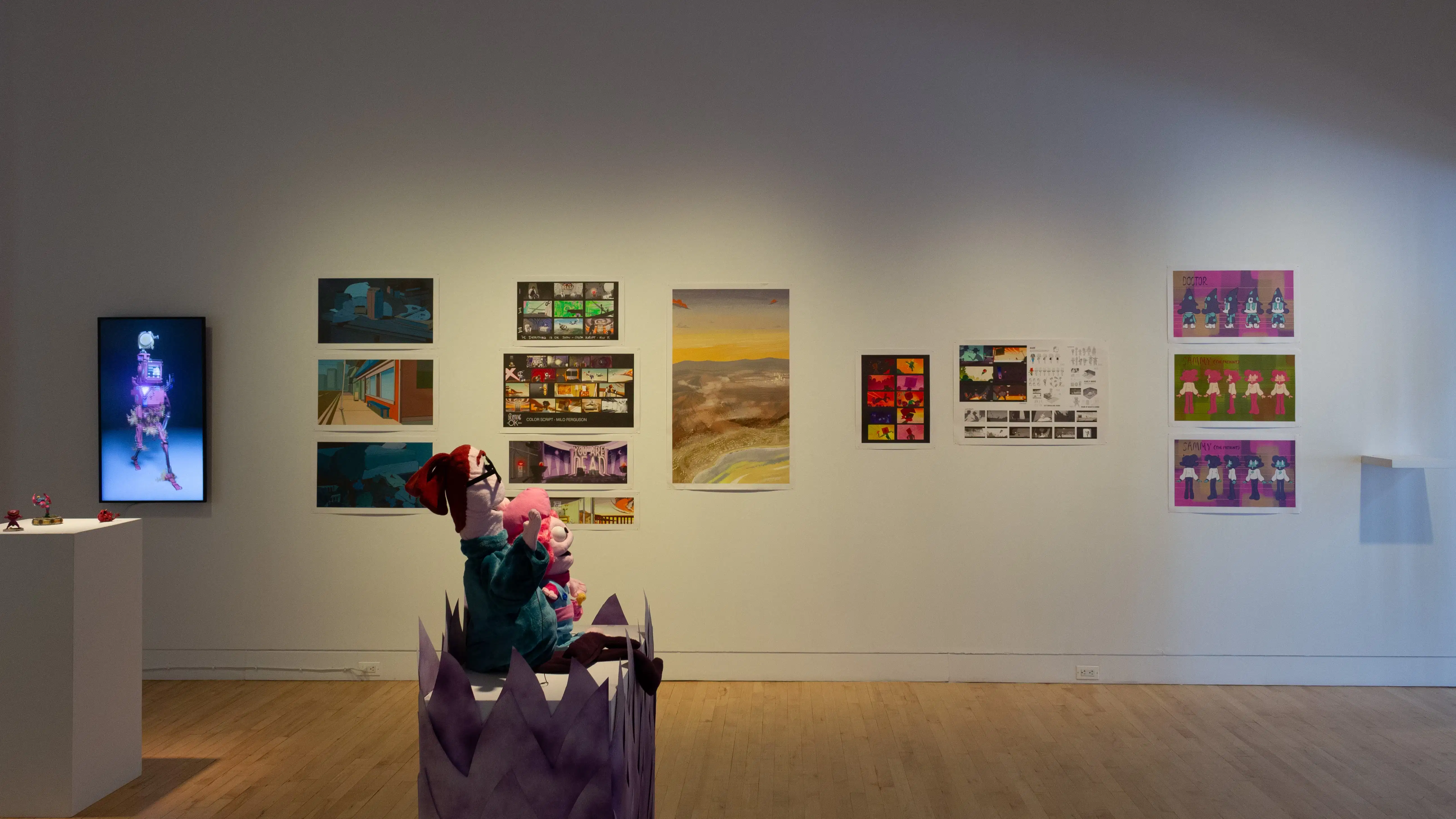 Installation image showing a straight-on view of a print-lined wall with pedestals in the center of the floor.