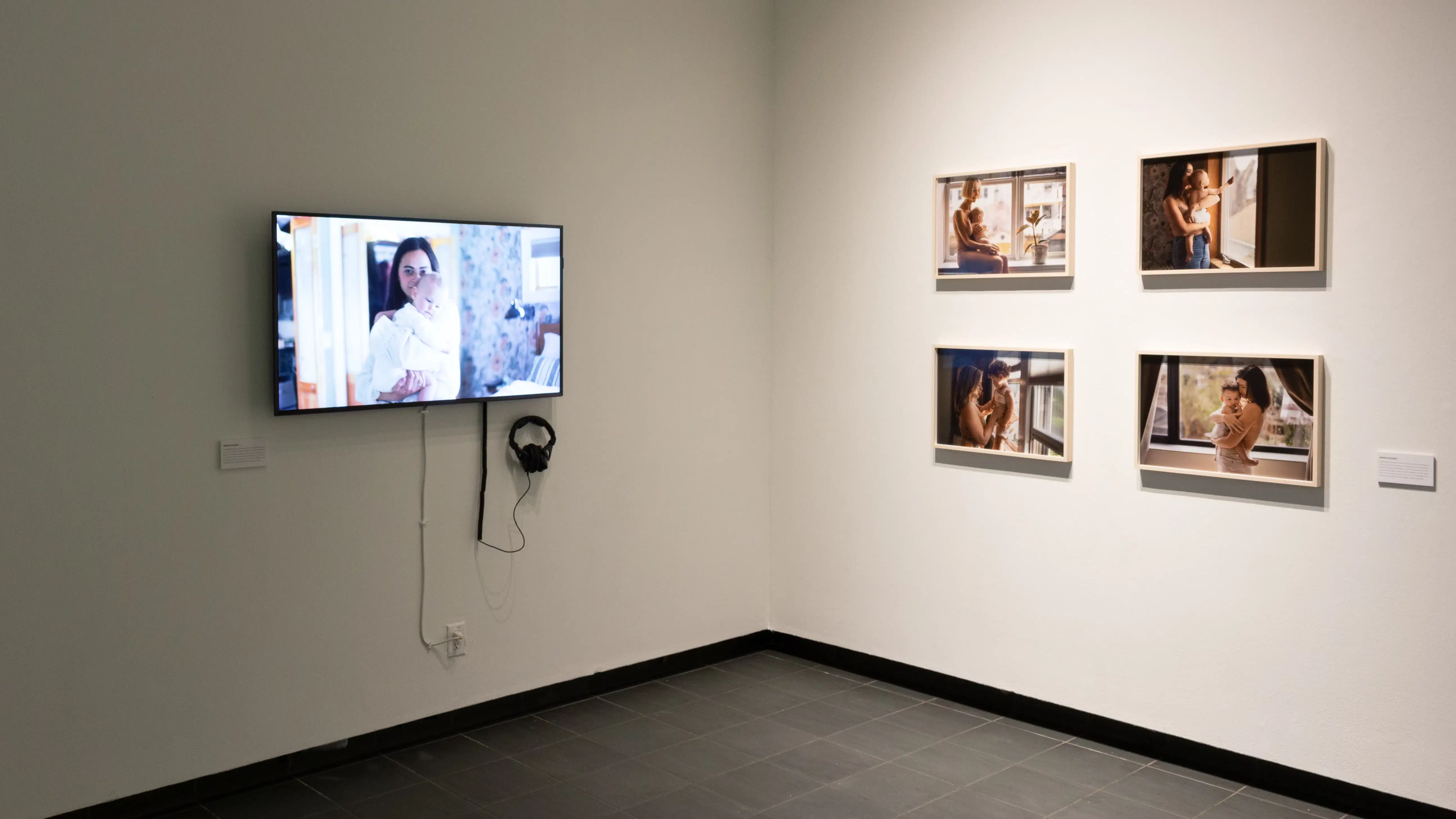 In one corner of the gallery, a video about motherhood plays on a monitor next to four photographs of mothers and their babies.