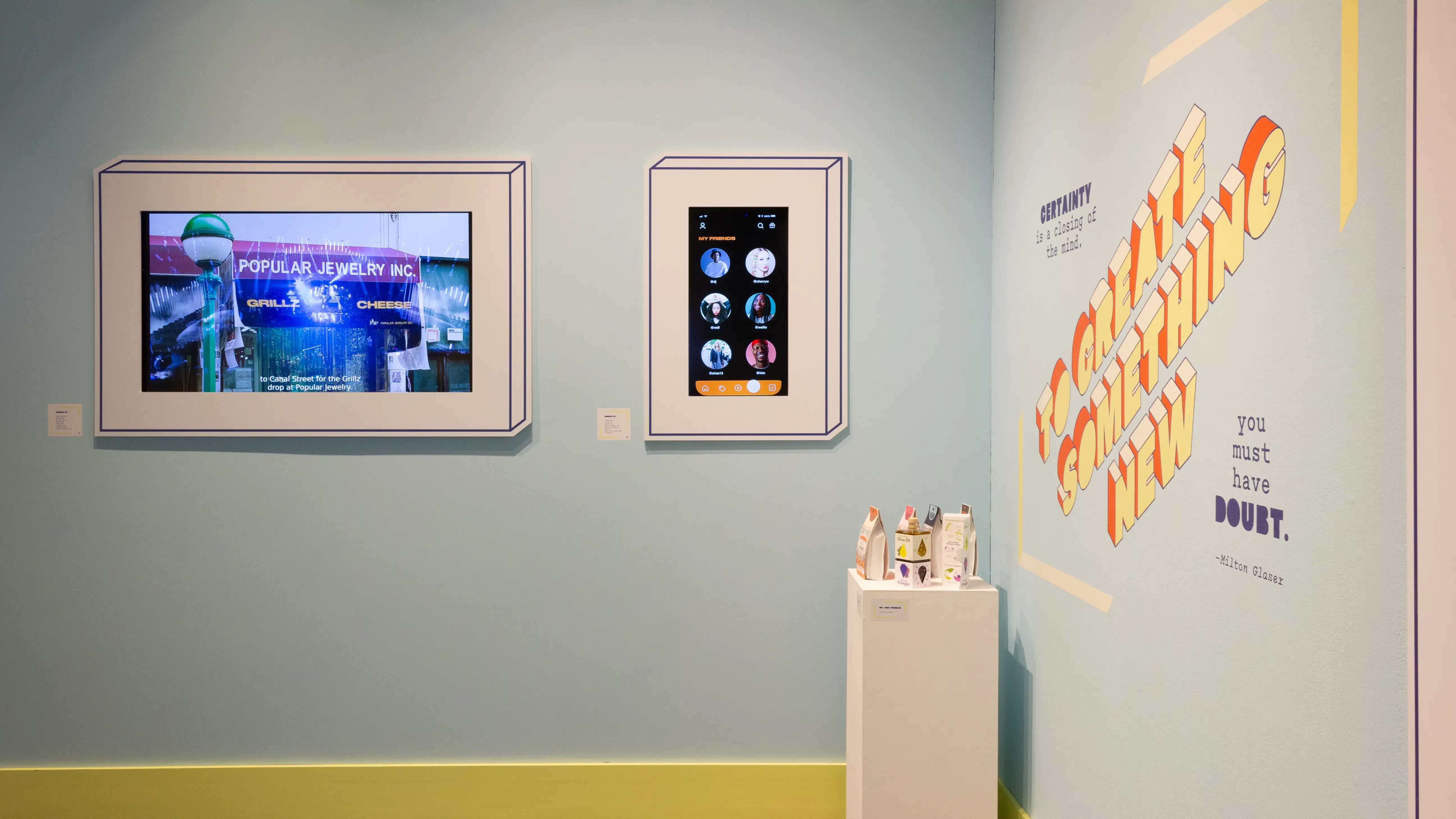 A straight view of the corner in the alcove, without the mannequins in view. There is a podium displaying several small objects and two brightly-lit monitors on the opposing wall.