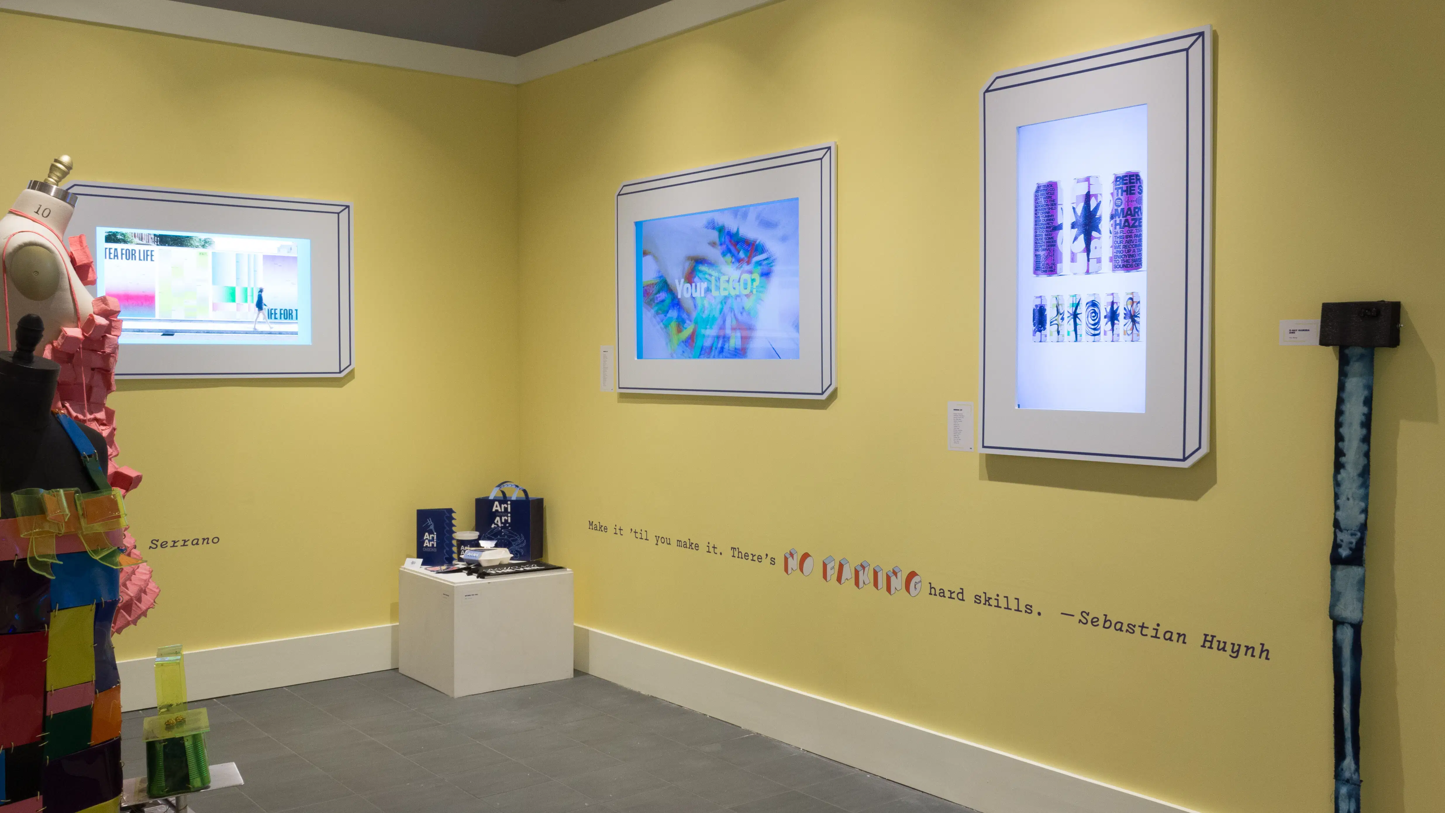 Angled view of a corner, with a small pedestal in the corner, two monitors on one wall and one monitor visible on the opposing wall.