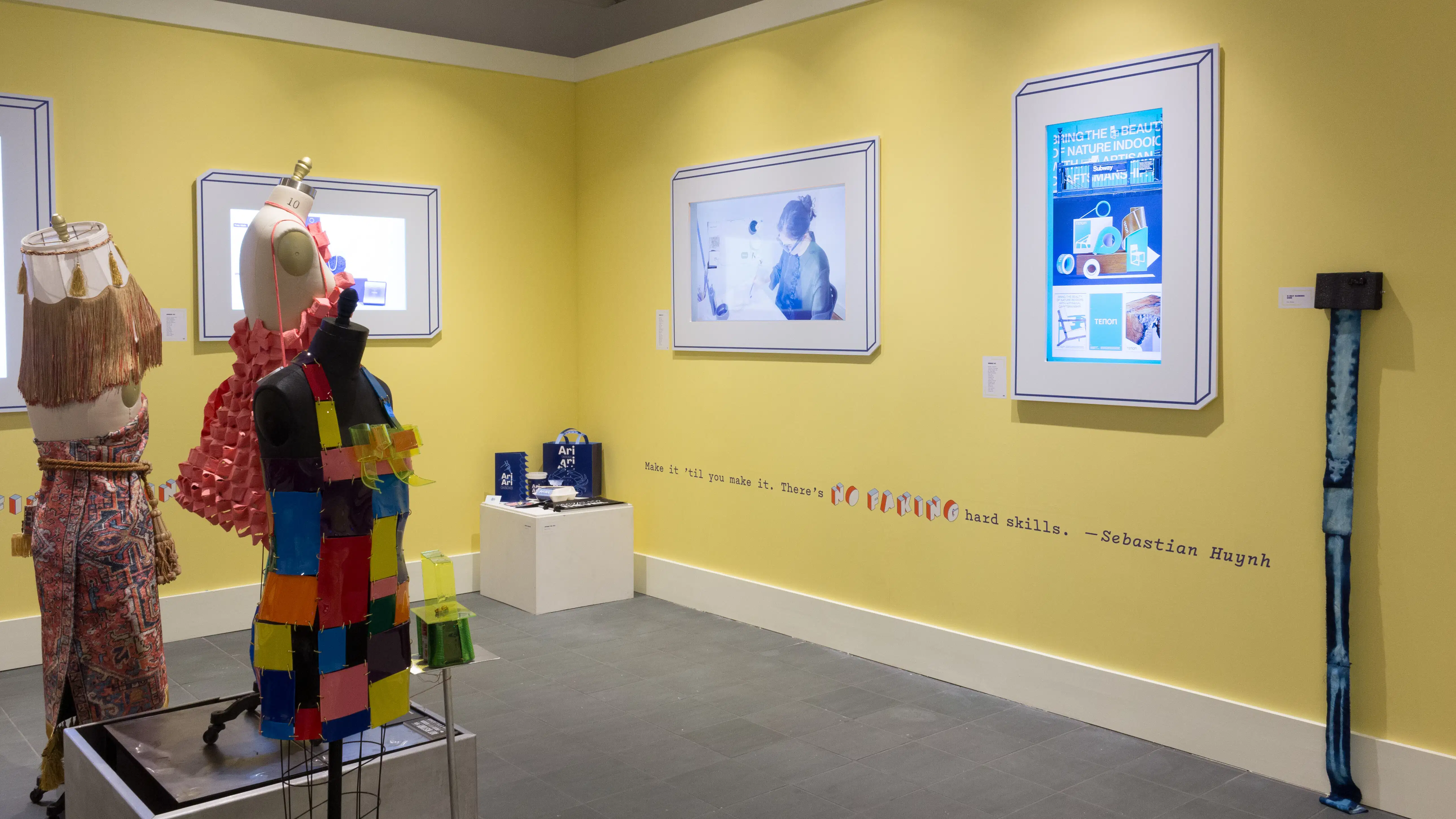 Angled view of a corner, with a small pedestal in the corner, two monitors on one wall and one monitor visible on the opposing wall. Three mannequins can be seen on the left.