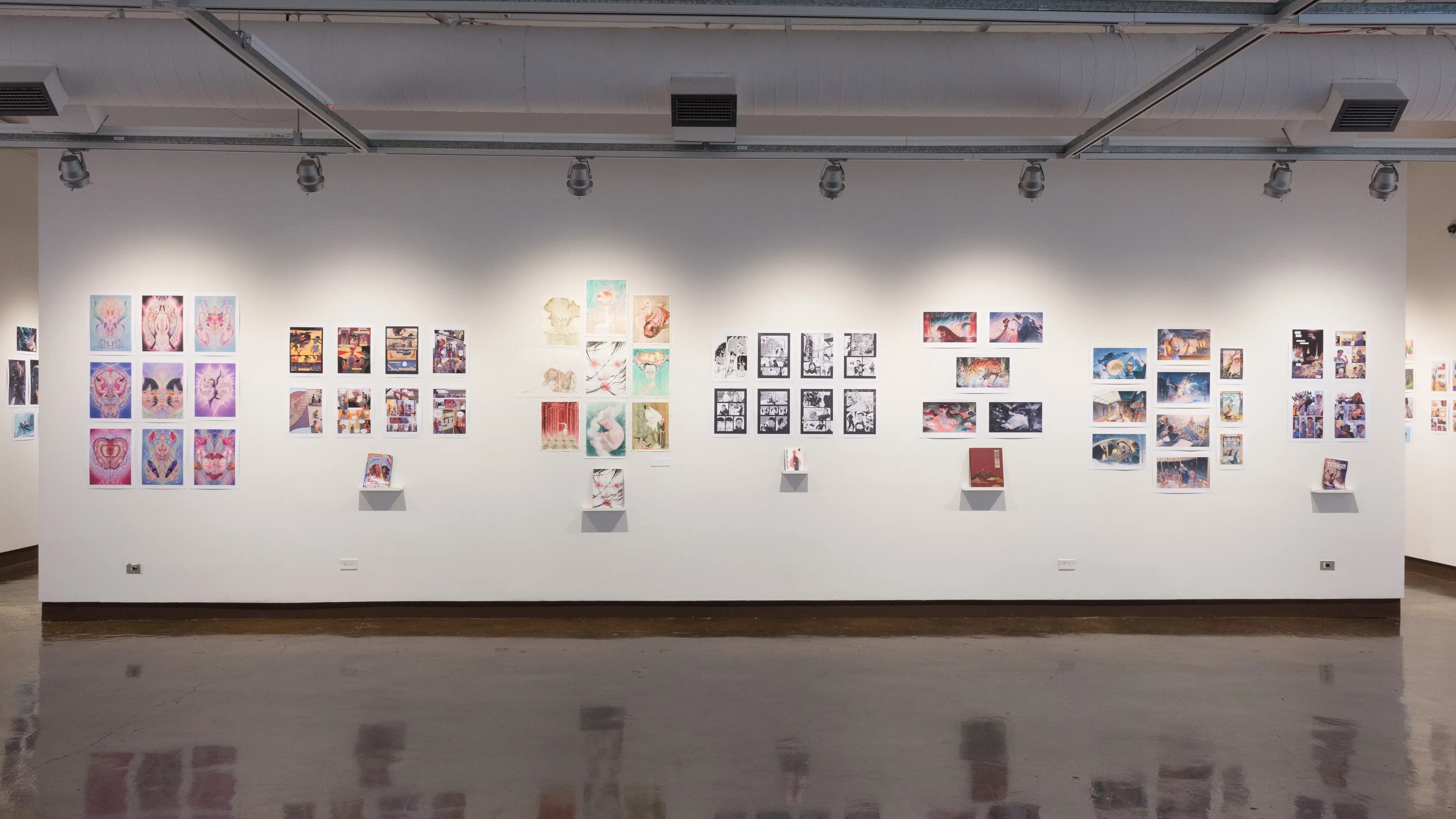 A wall in the first gallery space of the SVA Chelsea Gallery holds seven separate student projects. Each project is displayed as a book on a shelf, with prints from the book hung on the wall above it.