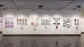 A wall in the first gallery space of the SVA Chelsea Gallery holds seven separate student projects. Each project is displayed as a book on a shelf, with prints from the book hung on the wall above it.