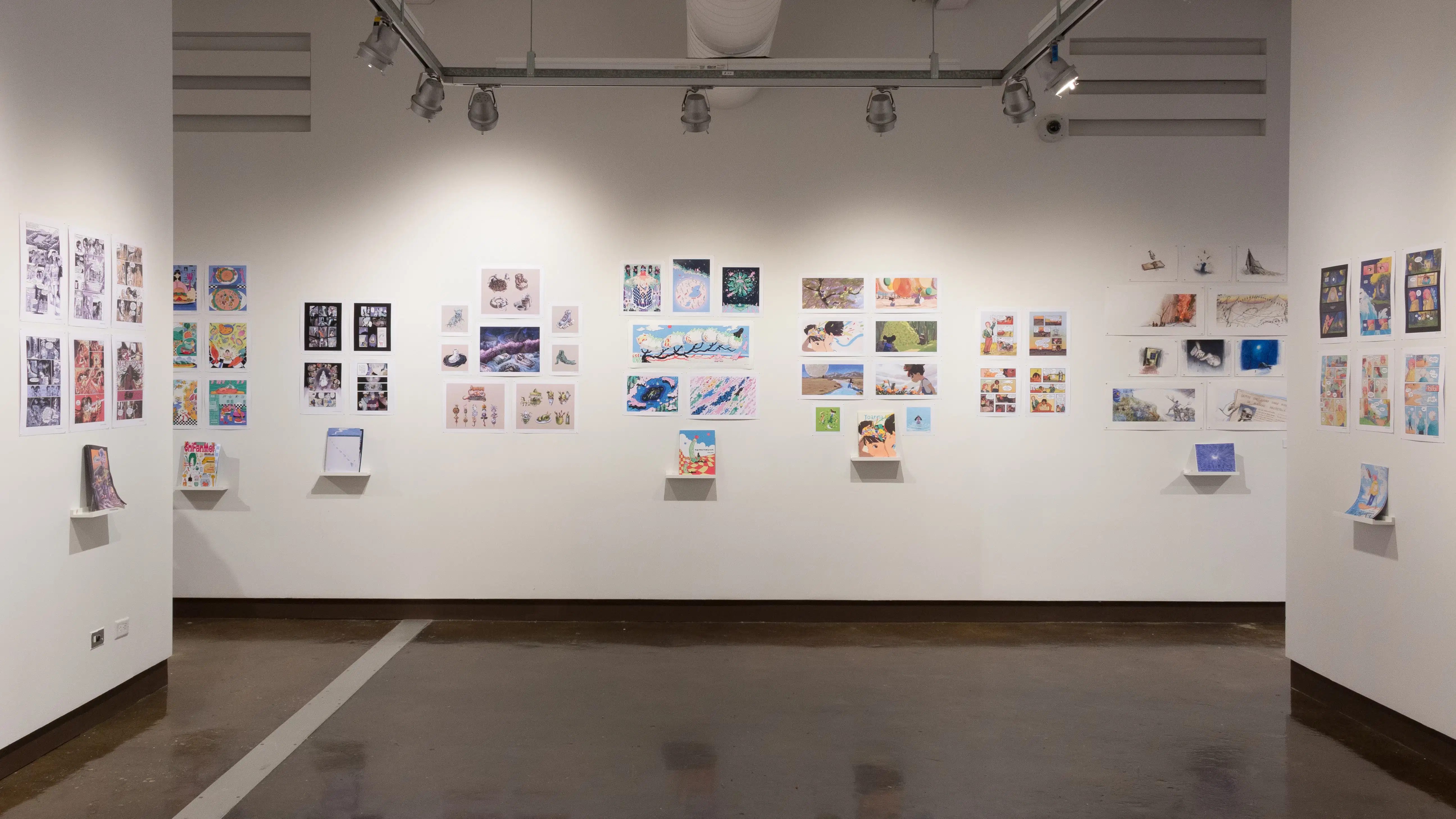 Students’ illustrated books are displayed on shelves, with prints from the books hanging on the wall above.
