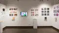 In the alcove of the third gallery space, more student work is displayed in the form of prints and books. However, there is also a monitor playing animations, and a pedestal holding some ceramic sculptures of fried eggs.