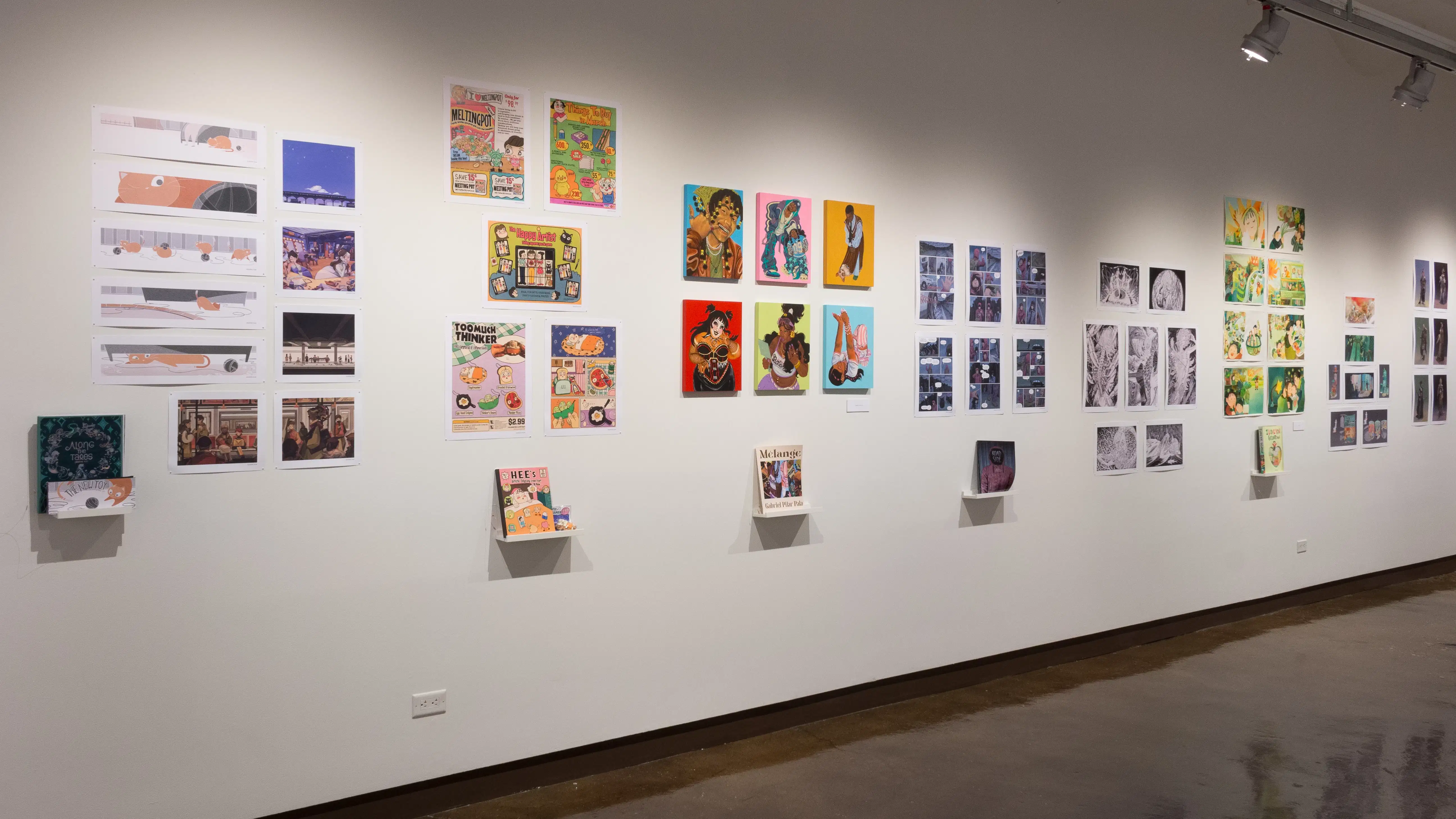 Prints, originals, and books are all displayed on a wall of gallery three.