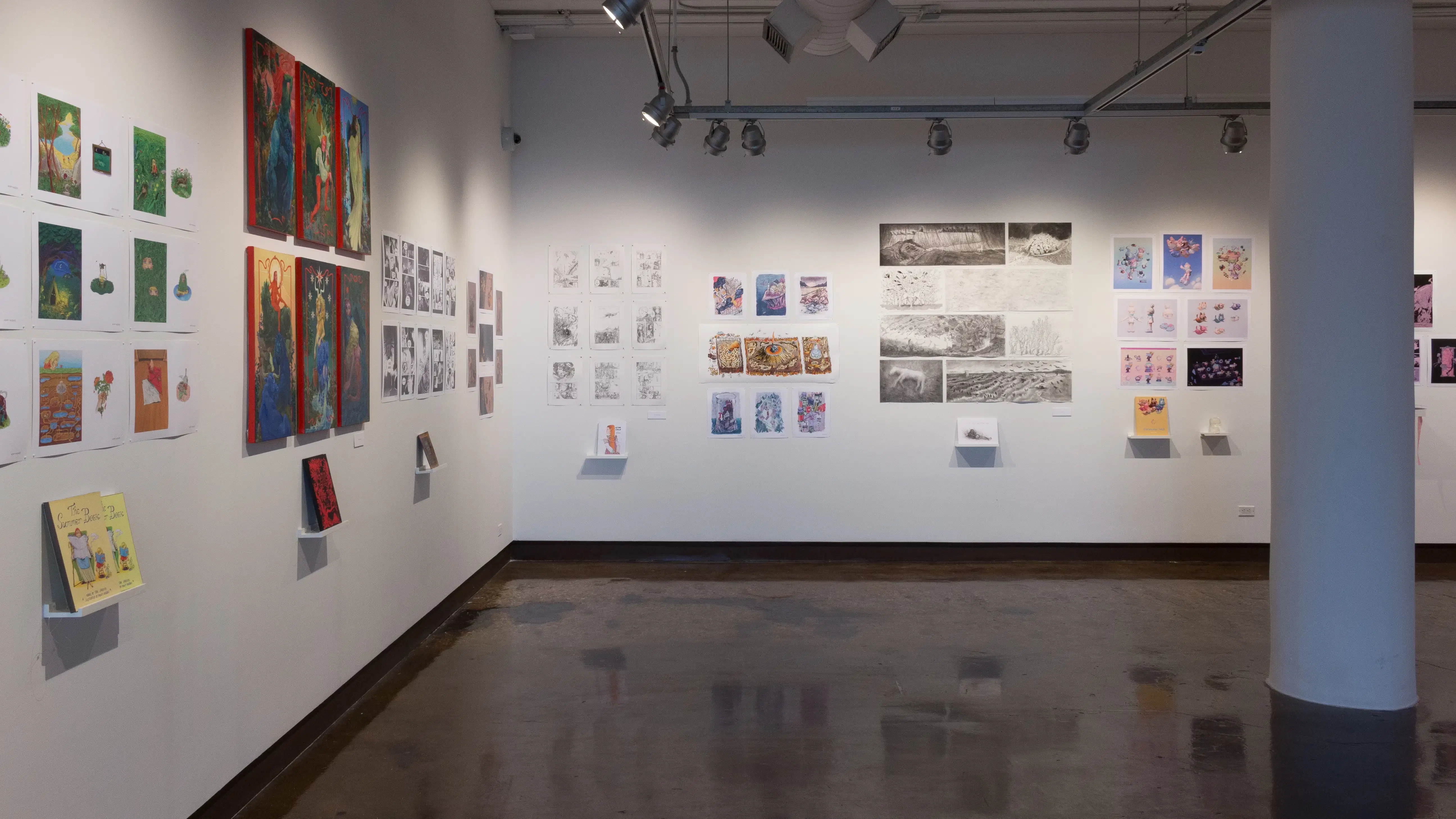 Back in the first gallery space, the prints and originals hanging on the walls vary in dimension, style, and color. Books sit on shelves beneath the prints or originals.