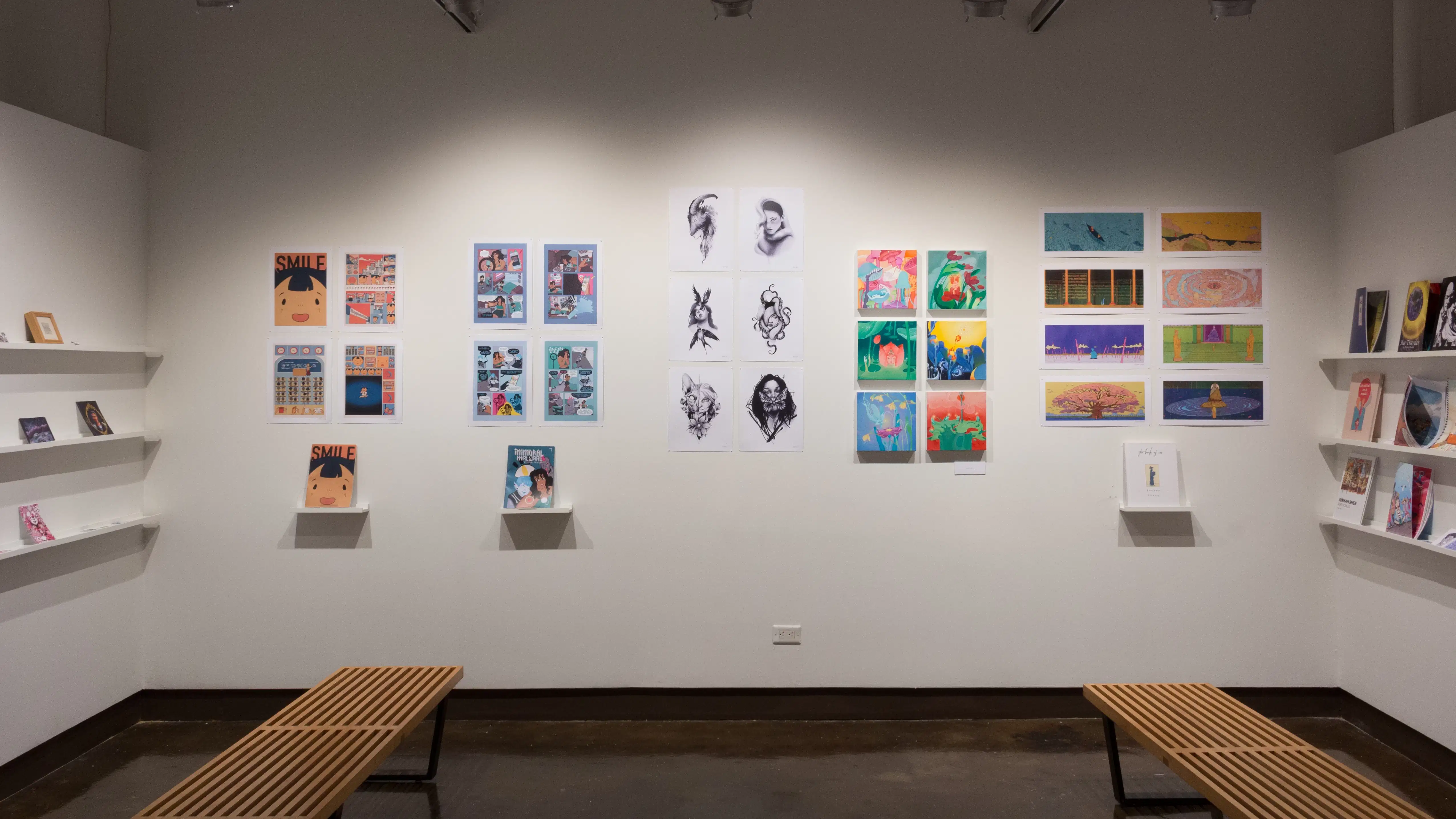 In the alcove of gallery four, the two side walls have shelves which hold students’ books. On the center wall, prints, originals, and books are displayed.