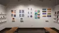 In the alcove of gallery four, the two side walls have shelves which hold students’ books. On the center wall, prints, originals, and books are displayed.