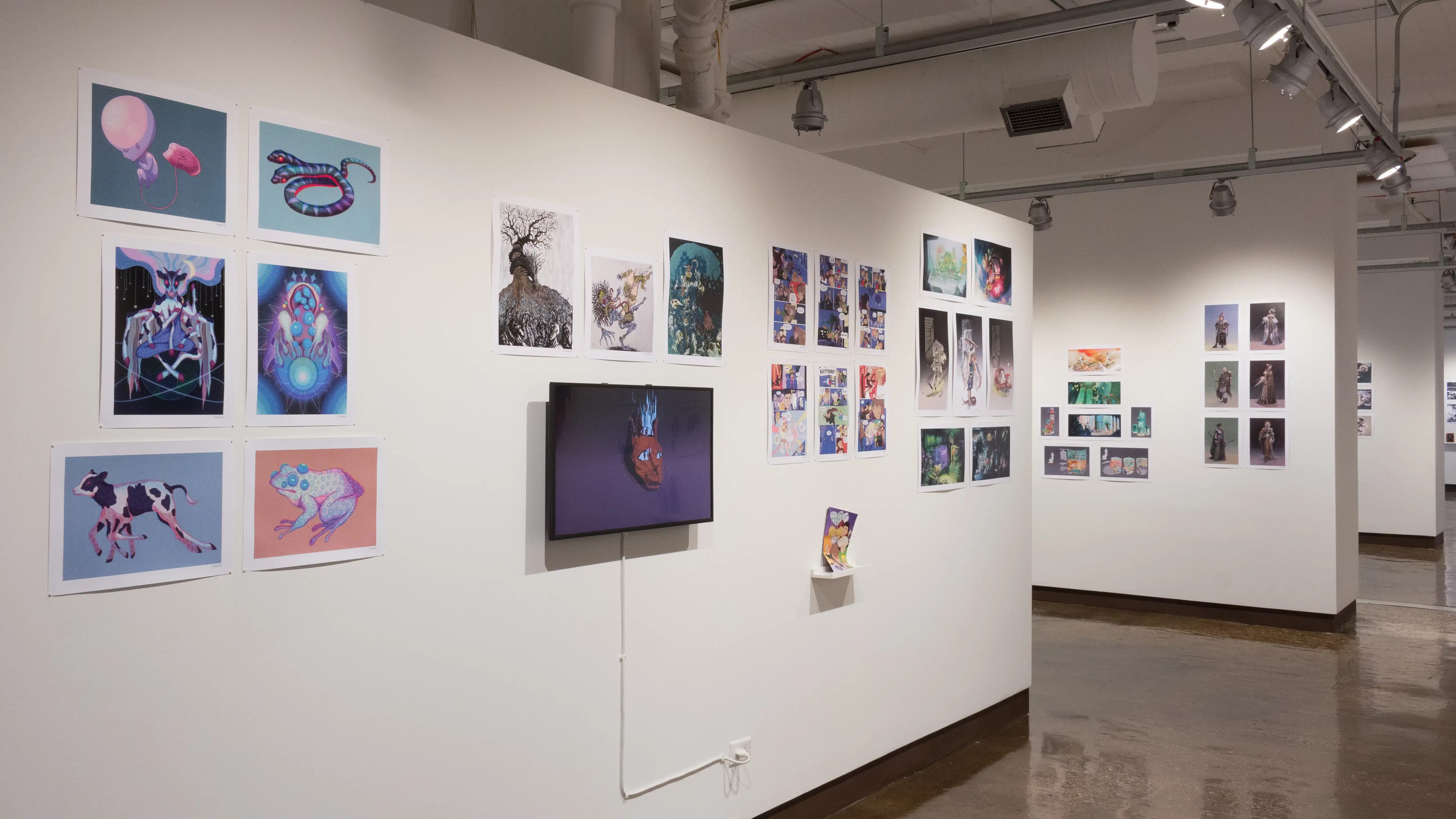 The prints hanging on the walls vary in dimension, style, and color. A monitor displaying an animation hangs in the middle of the wall, surrounded by the prints.