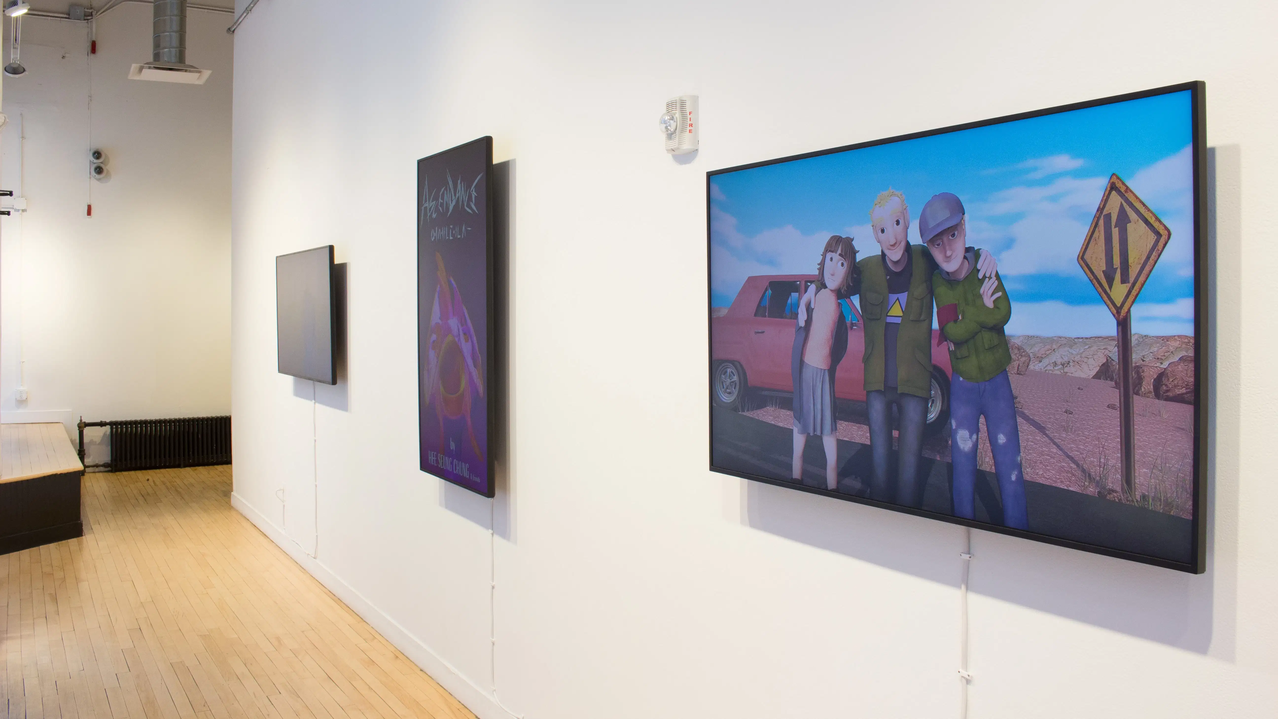 Angled view of three monitors, one vertical monitor flanked by two horizontal monitors, displaying animated videos from students.