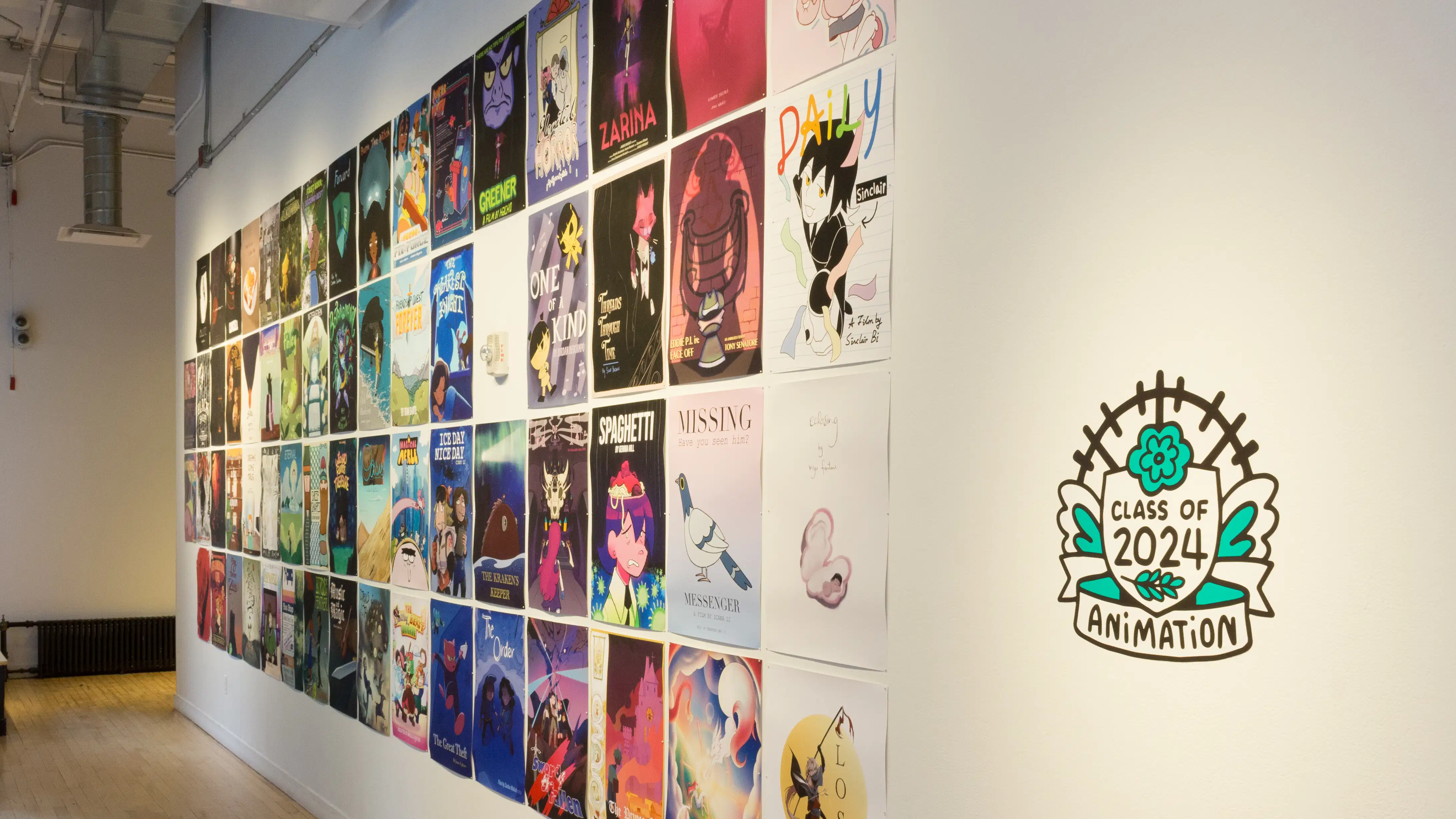 ny posters hang in four rows on a white gallery wall. Each of the posters include illustrated designs and titles. Next to the posters, vinyl on the wall reads “Class of 2024 Animation”.