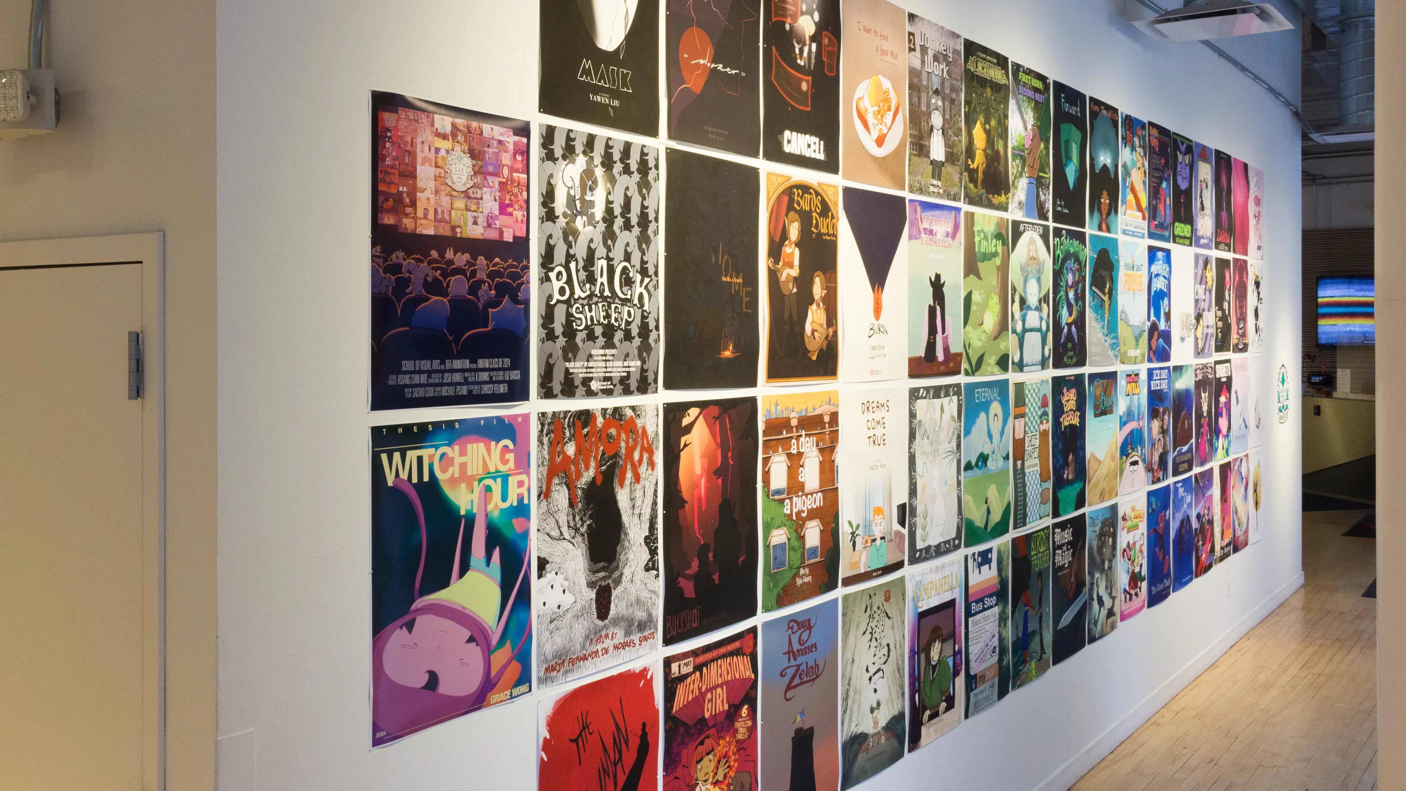 Four rows of colorful, illustrated posters are displayed in four rows on a white gallery wall. The posters are each about 11 x 14 inches.