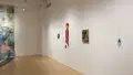 An angled view of the right wall in the SVA Flatiron Gallery, depicting colorful hanging sculpture pieces and paintings. 