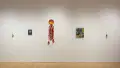 An even view of the right wall in the SVA Flatiron Gallery, displaying colorful hanging sculptures and various sized paintings. 